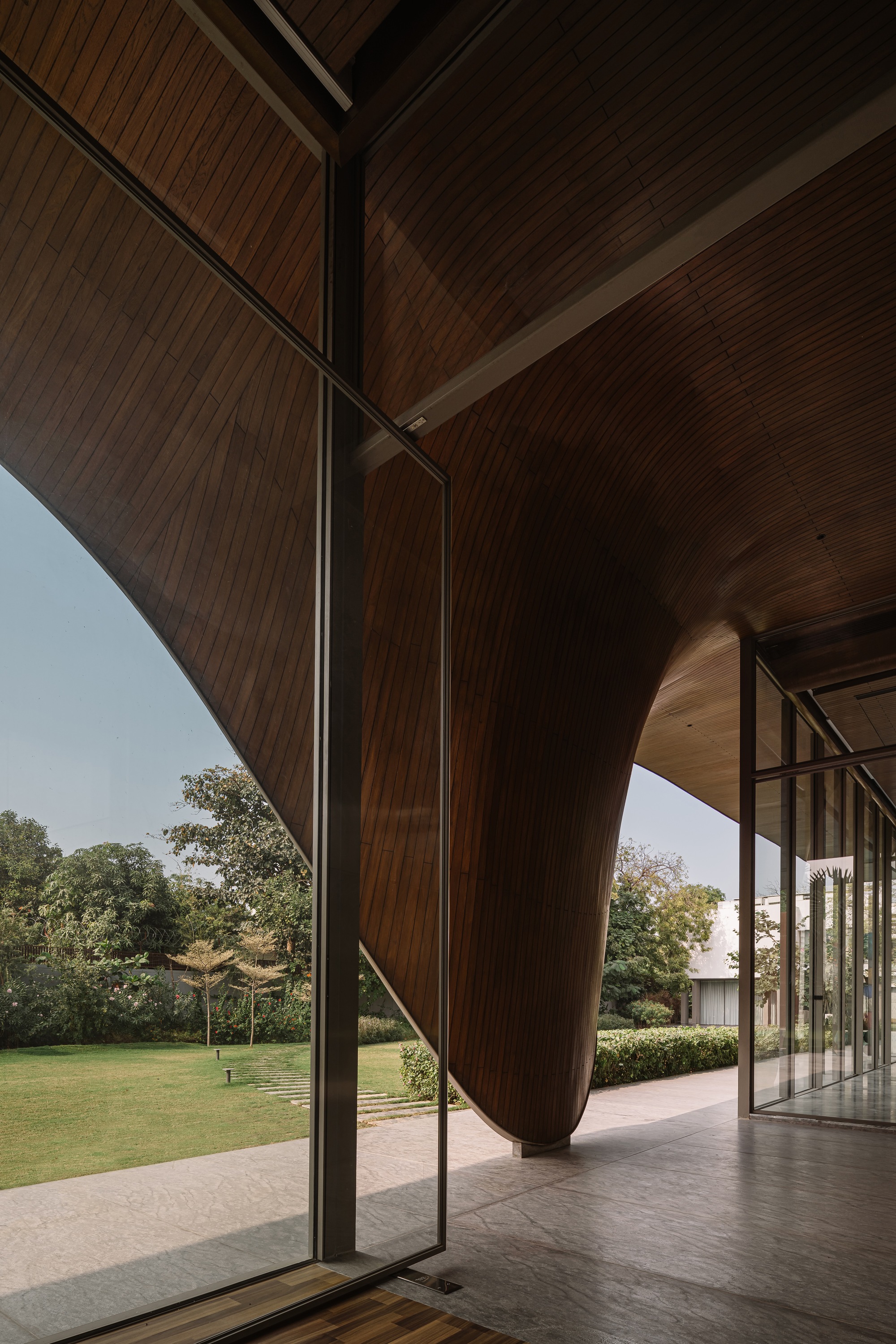 Interior view through open glass doors showing timber soffit curving down to meet polished concrete floor