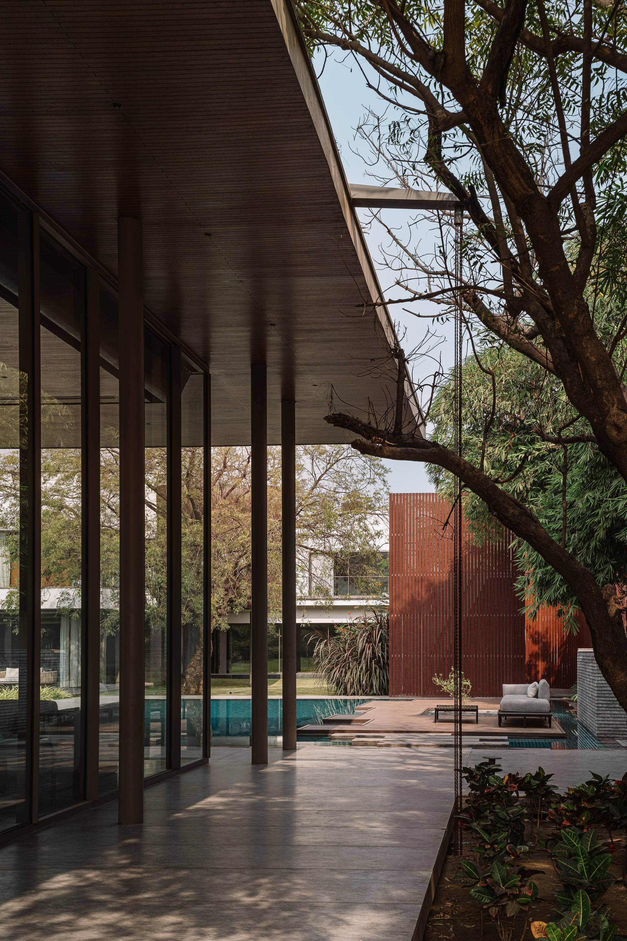 Covered terrace with dark timber columns and slatted ceiling opening to a courtyard pool and tree