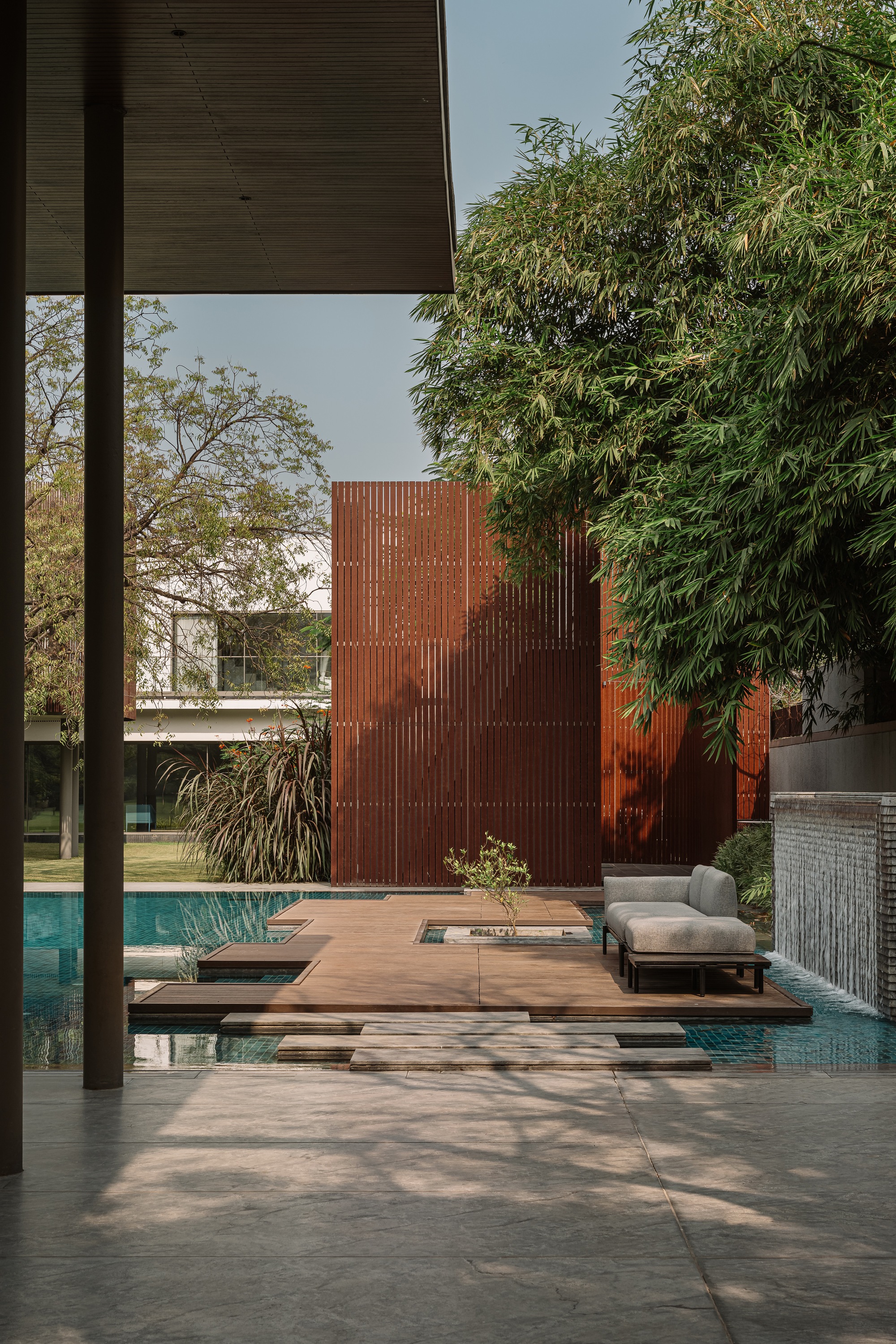 Timber deck platforms extending over the pool toward a perforated corten steel screen wall