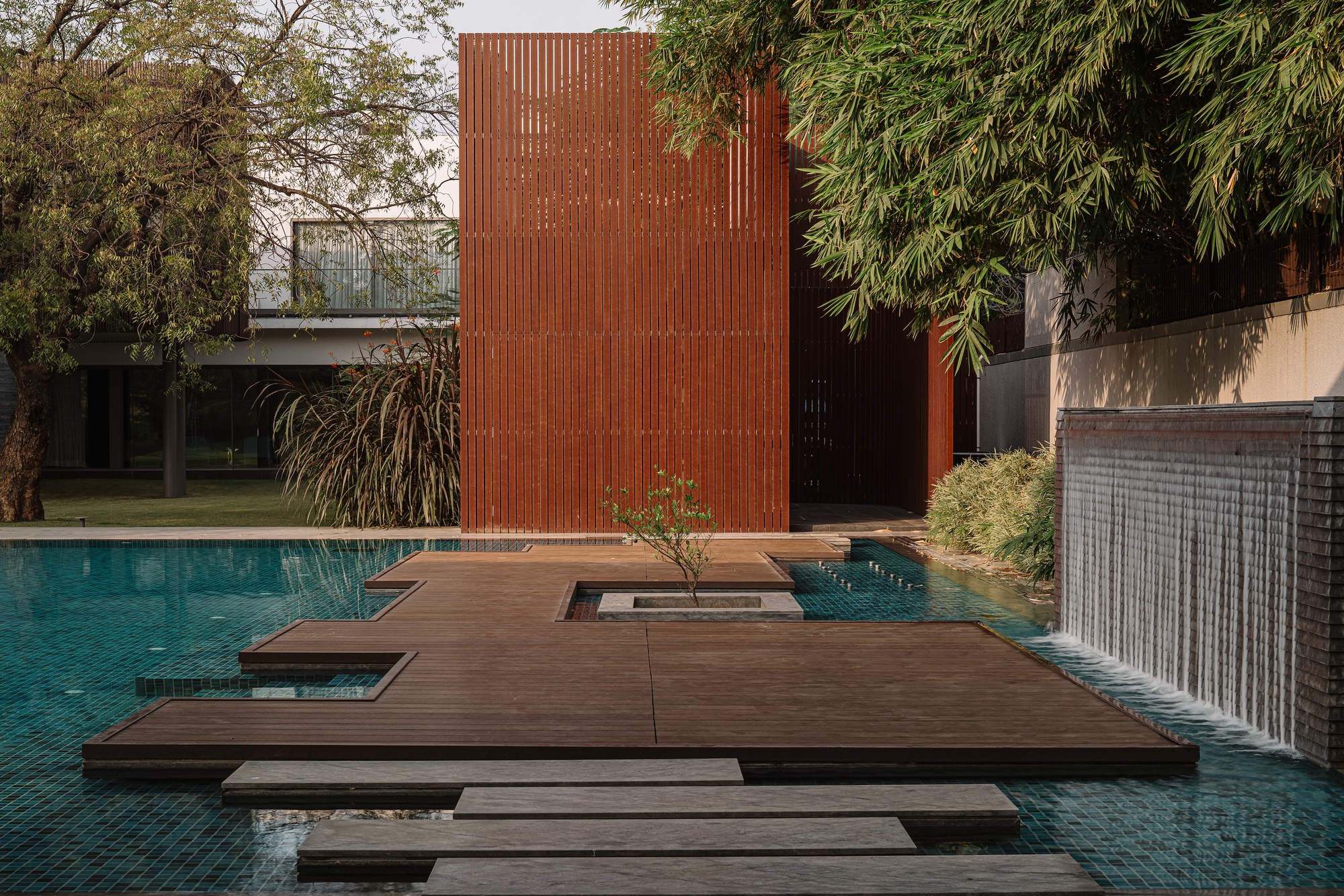 Floating timber deck with central planting cutout bridging the turquoise tiled pool beside a ribbed boundary wall