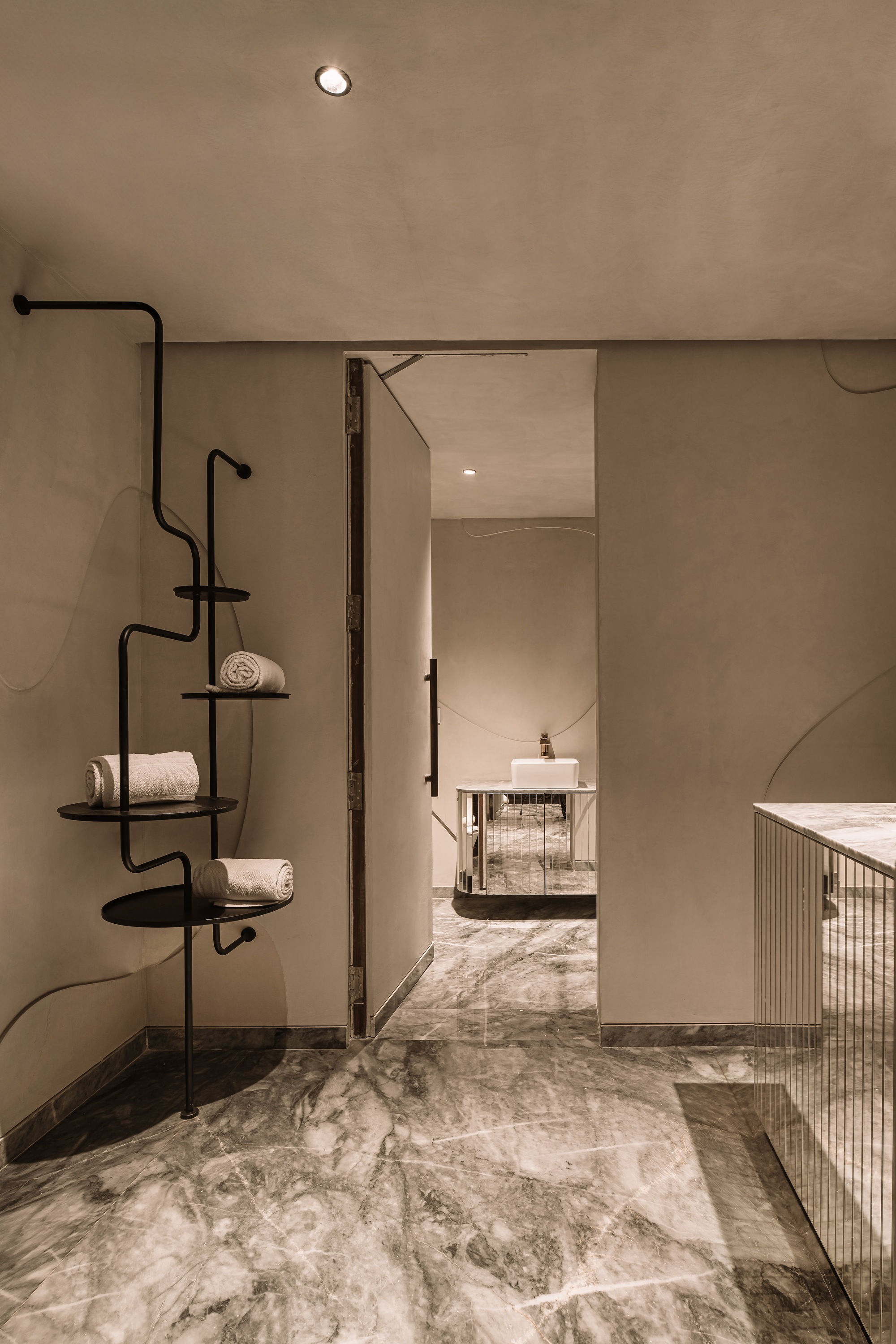 Interior threshold with black metal shelving unit beside grey marble floor and doorway to adjacent room