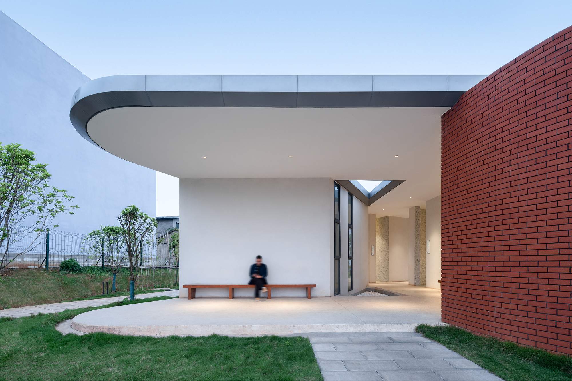 Covered entrance with curved canopy soffit between red brick wall and white interior hallway with person passing by