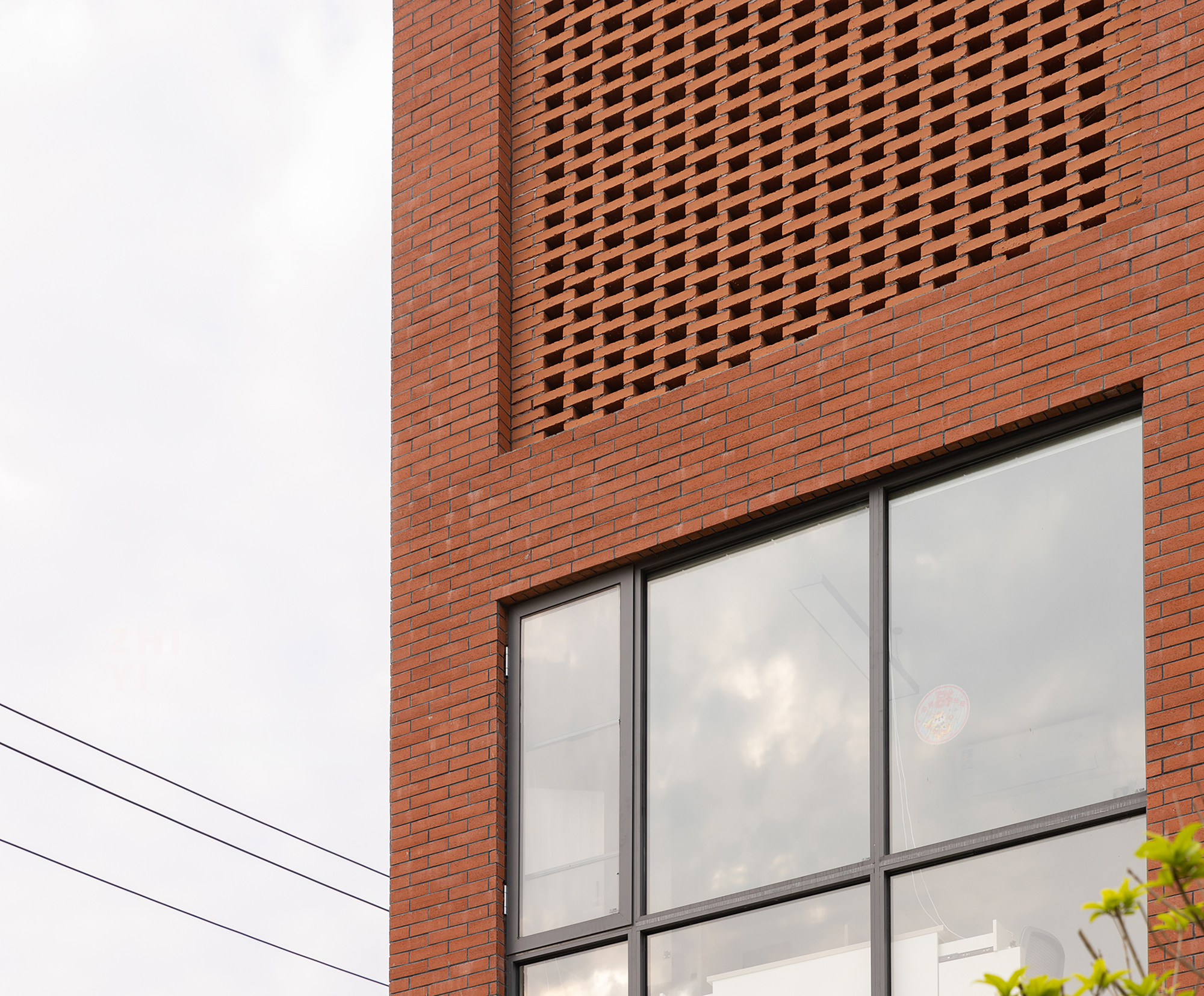 Detail of the red brick wall with perforated screen pattern above a large aluminum-framed window