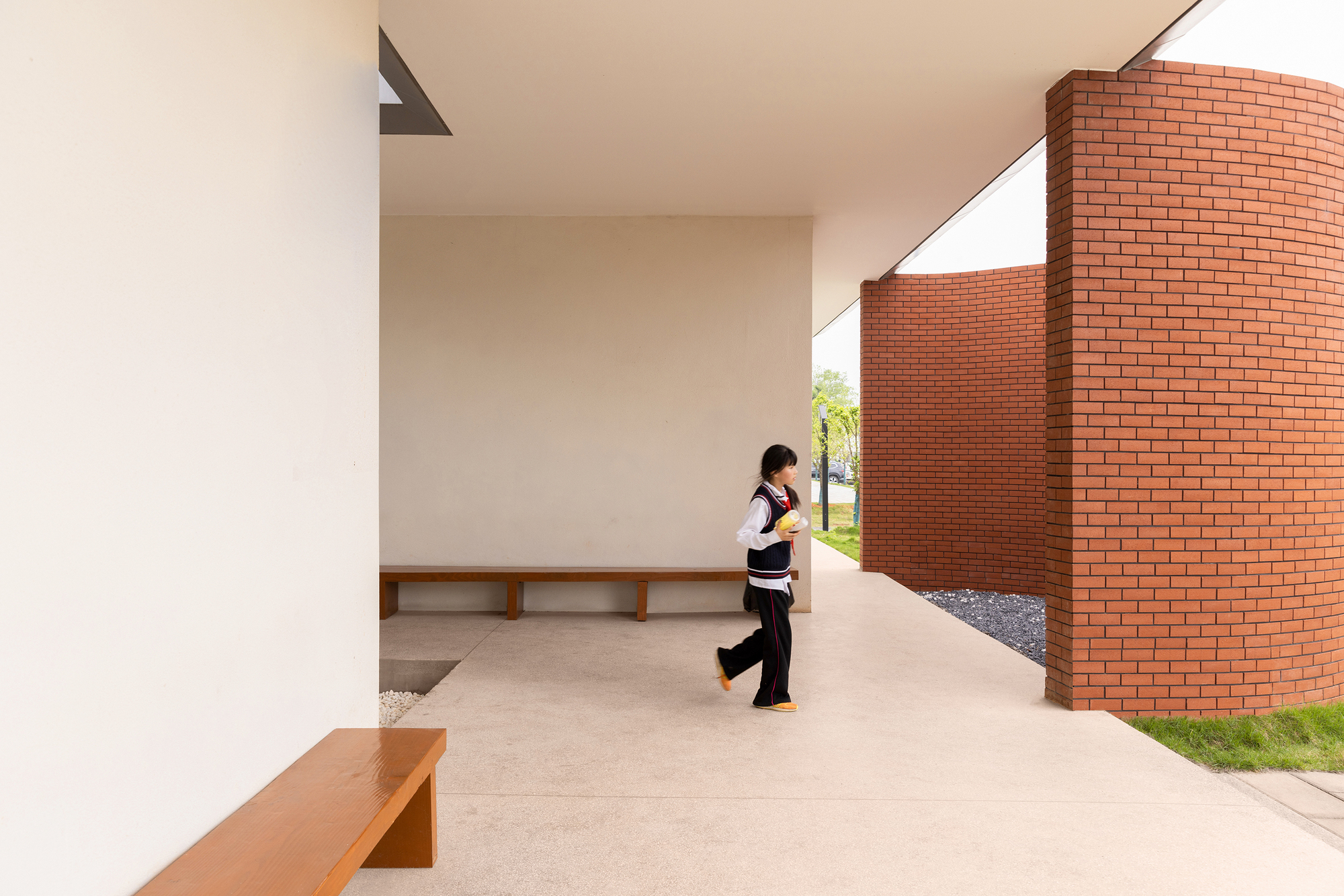 Covered walkway with a person walking past a curved red brick wall and built-in timber bench