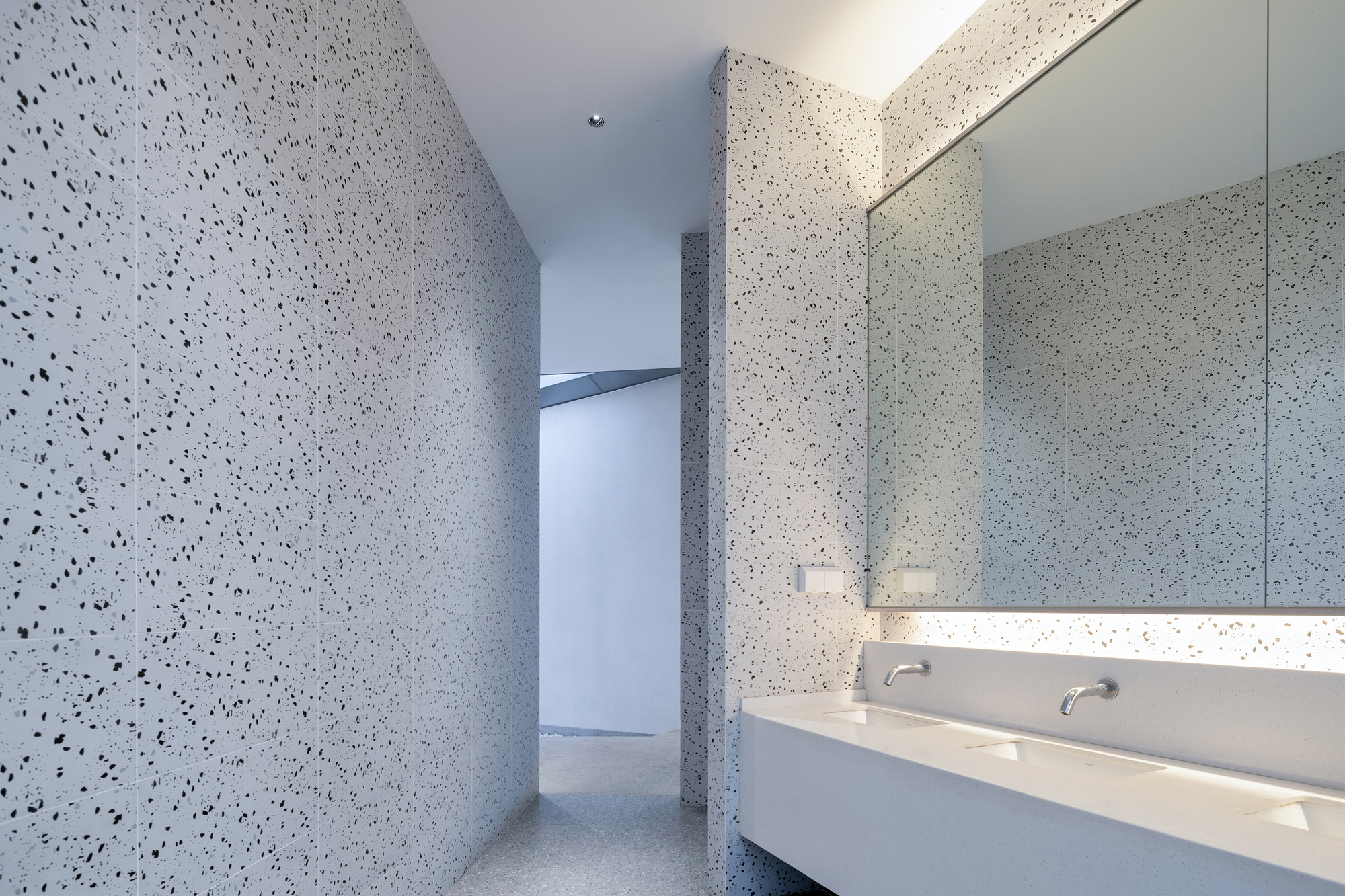 Bathroom interior with terrazzo walls, floating vanity and integrated strip lighting beneath the mirror
