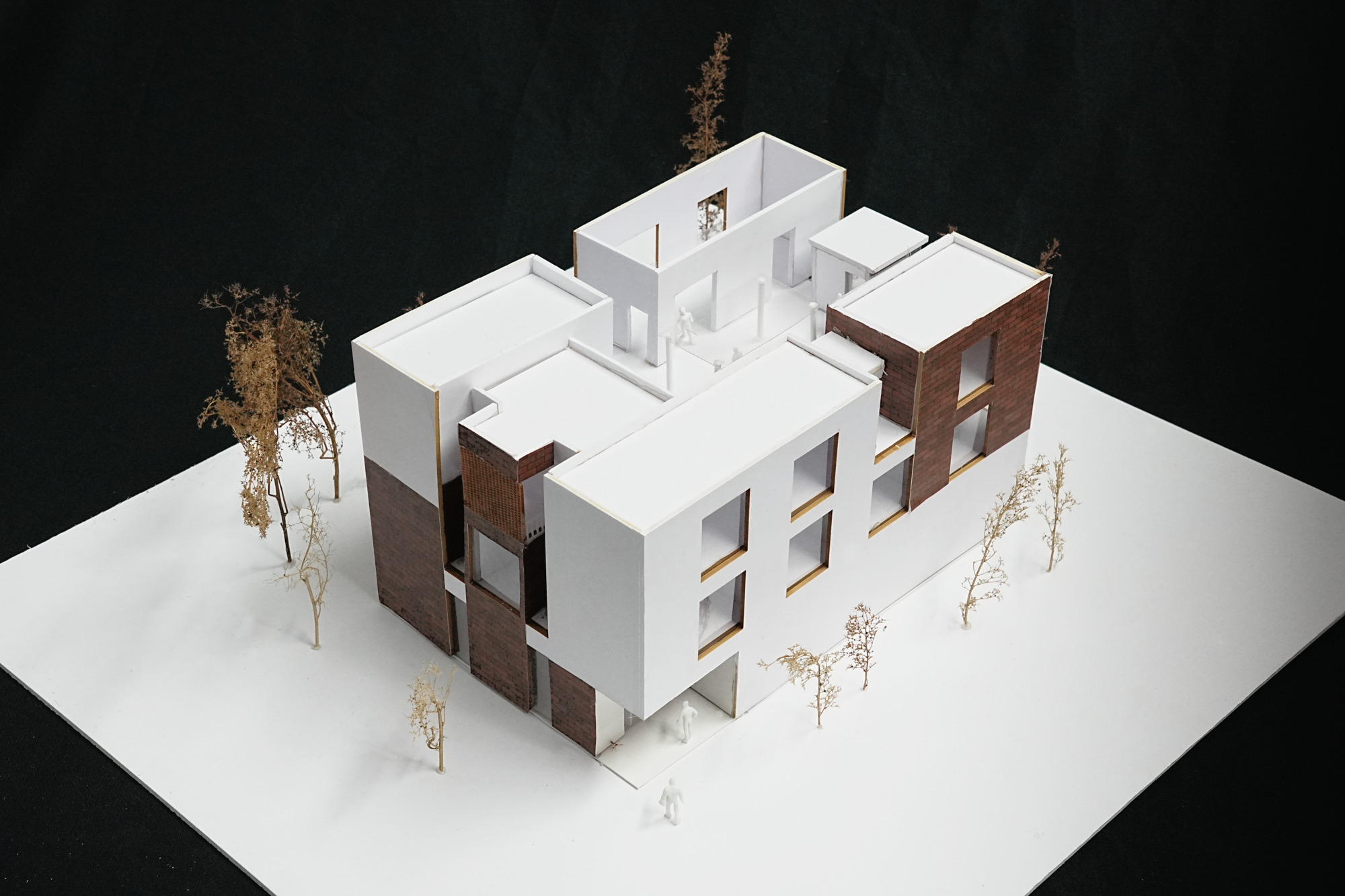Physical model showing clustered volumes with white and brick facades surrounded by miniature trees