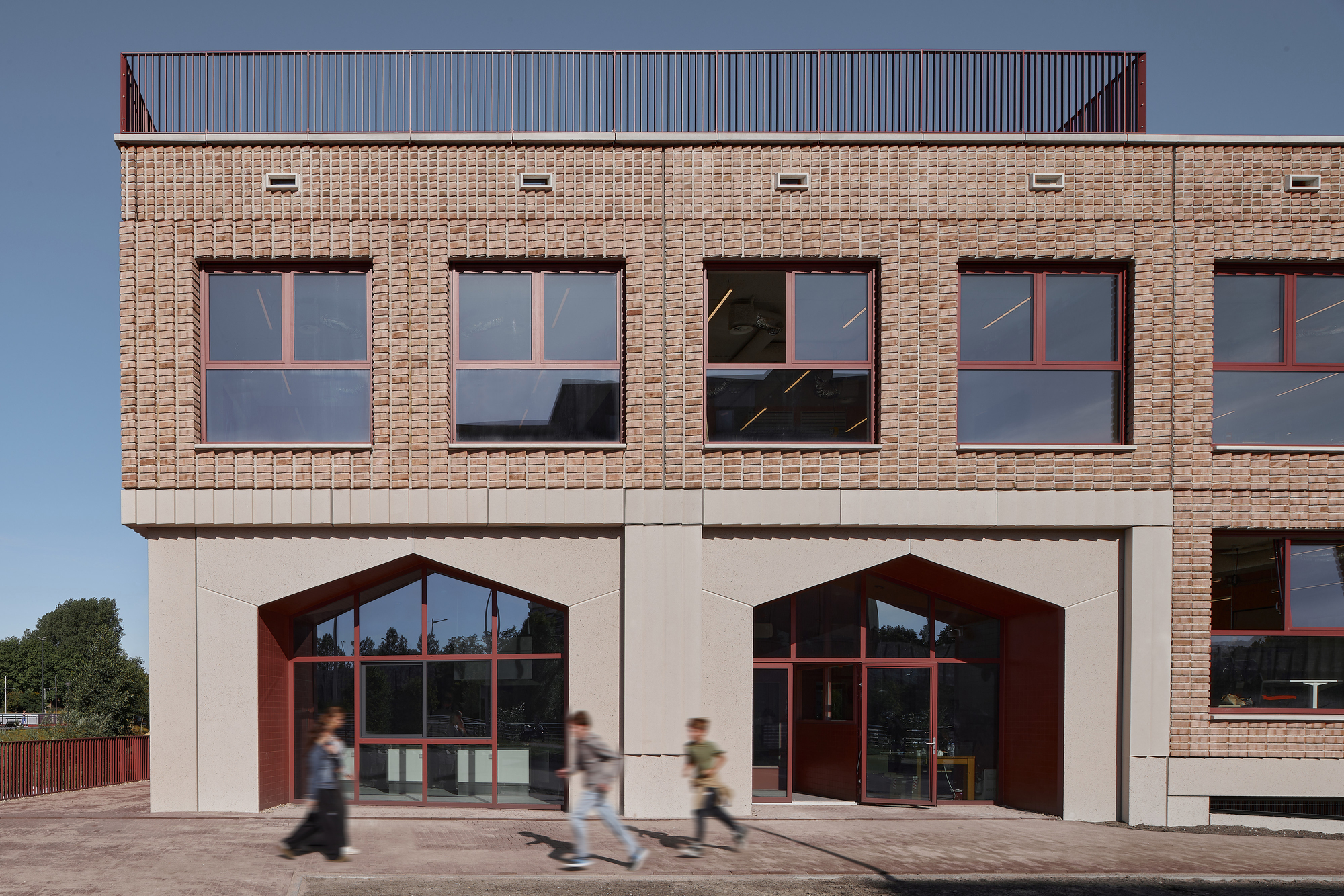 Street facade with buff brick upper story and white precast lower level featuring arched maroon-framed entrances