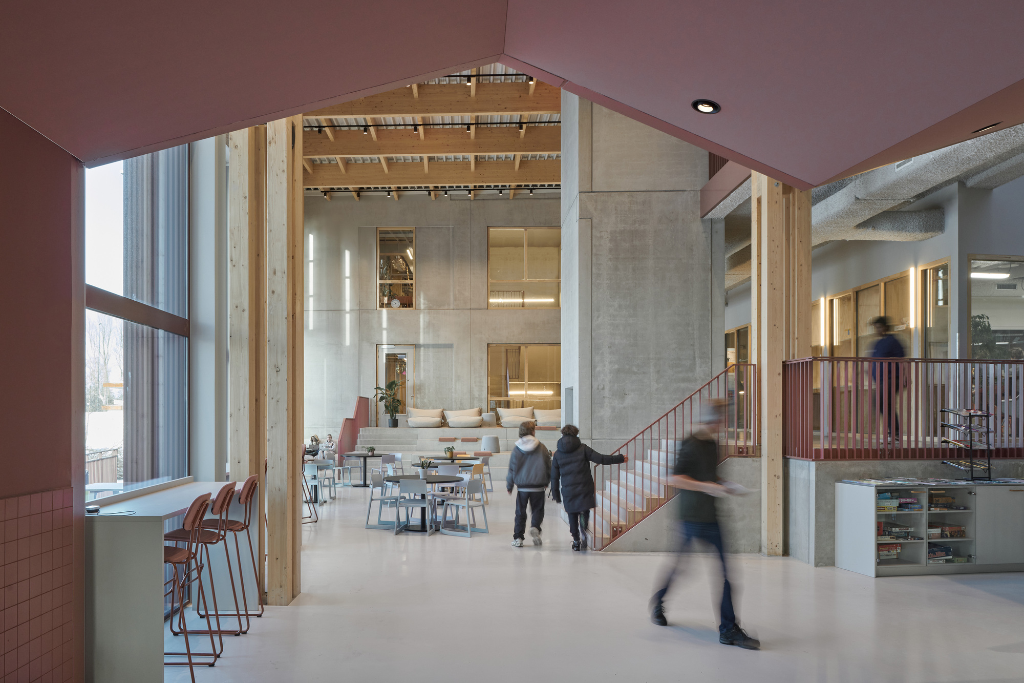 Double-height atrium with timber columns, concrete cores, and exposed timber ceiling beams with people moving through