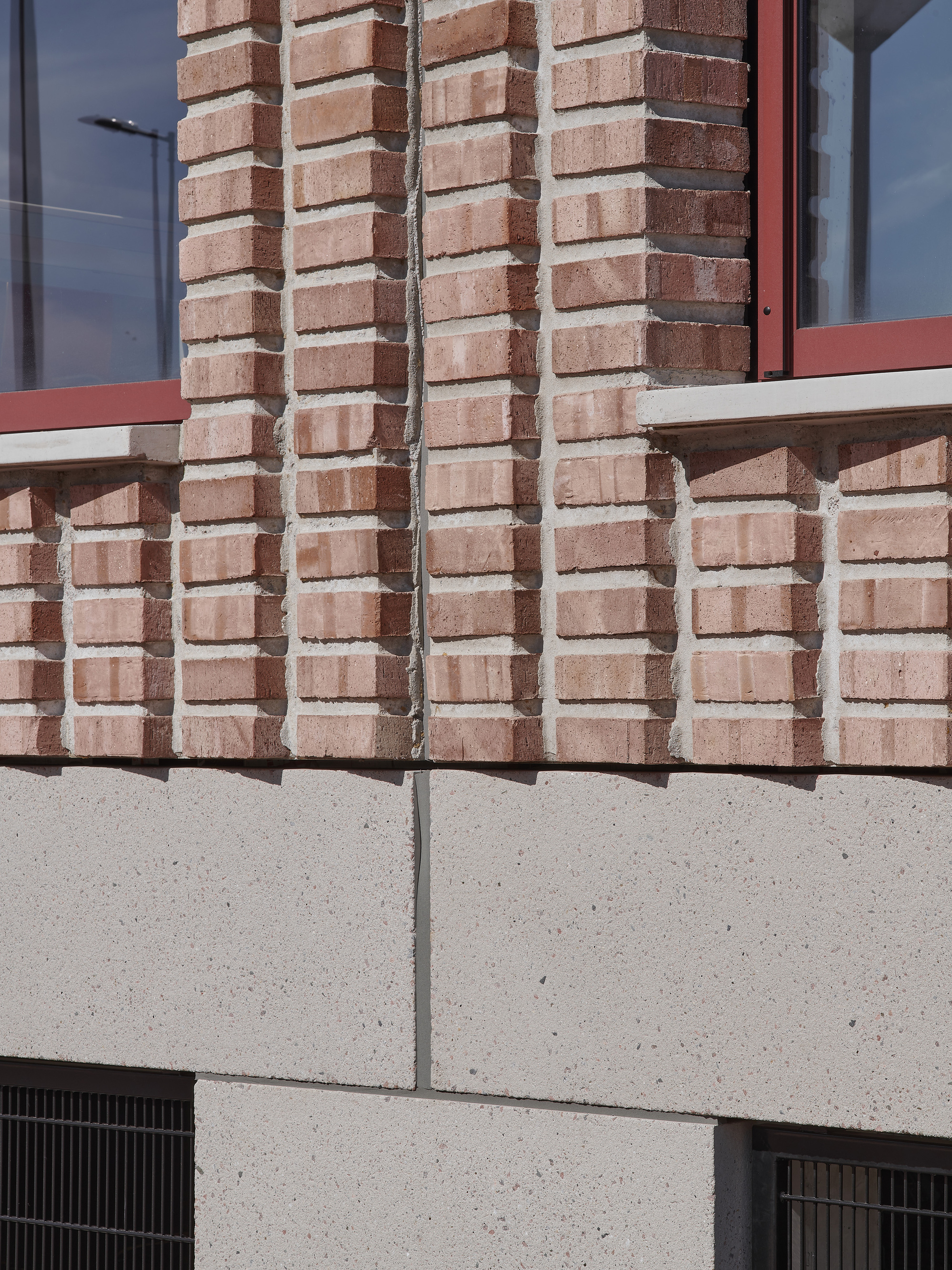 Detail of patterned brick pilasters meeting a concrete ledge above ventilation grilles in bright sunlight