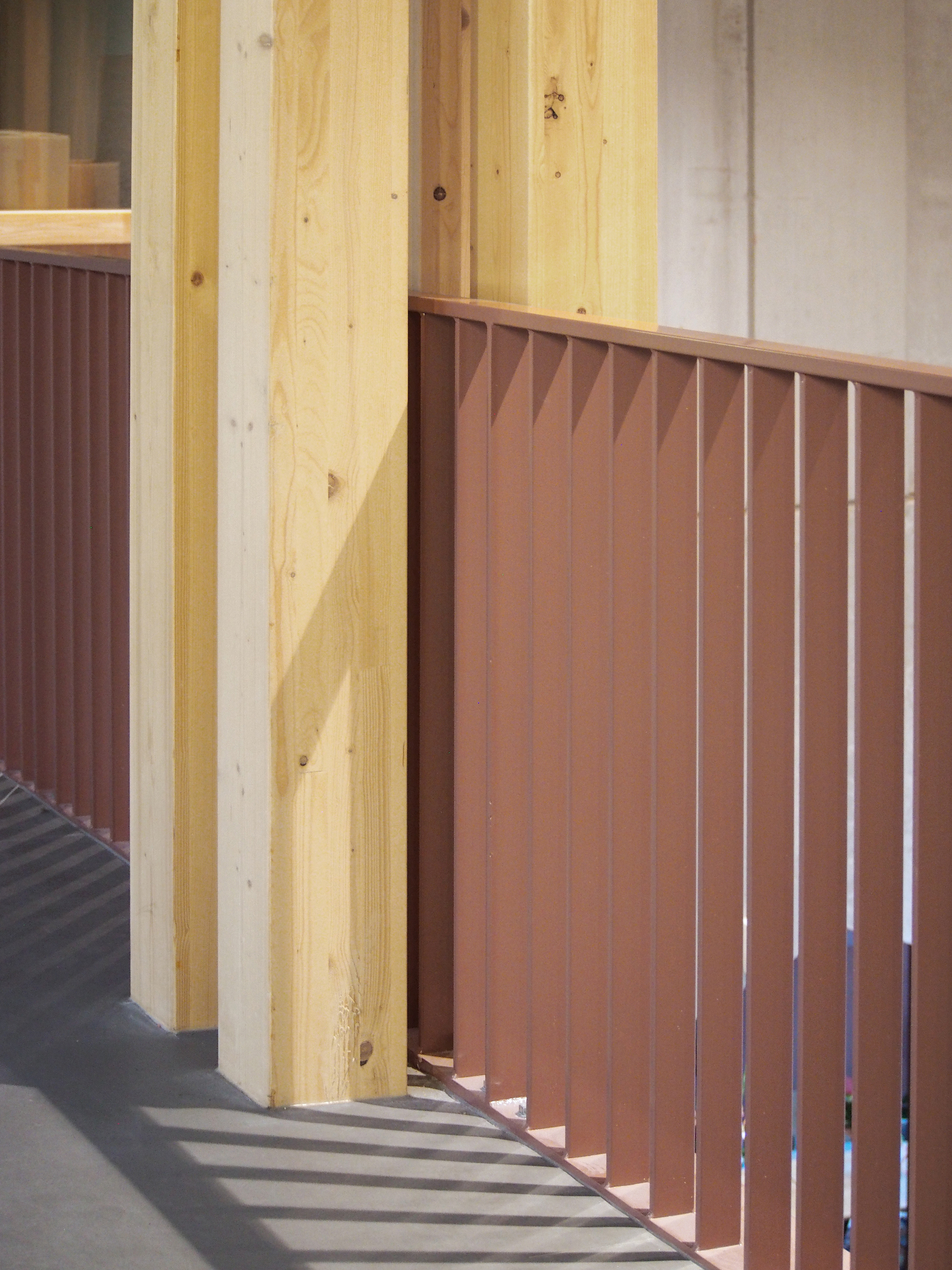 Corner detail showing timber column beside terracotta-colored vertical slat panel casting diagonal shadows