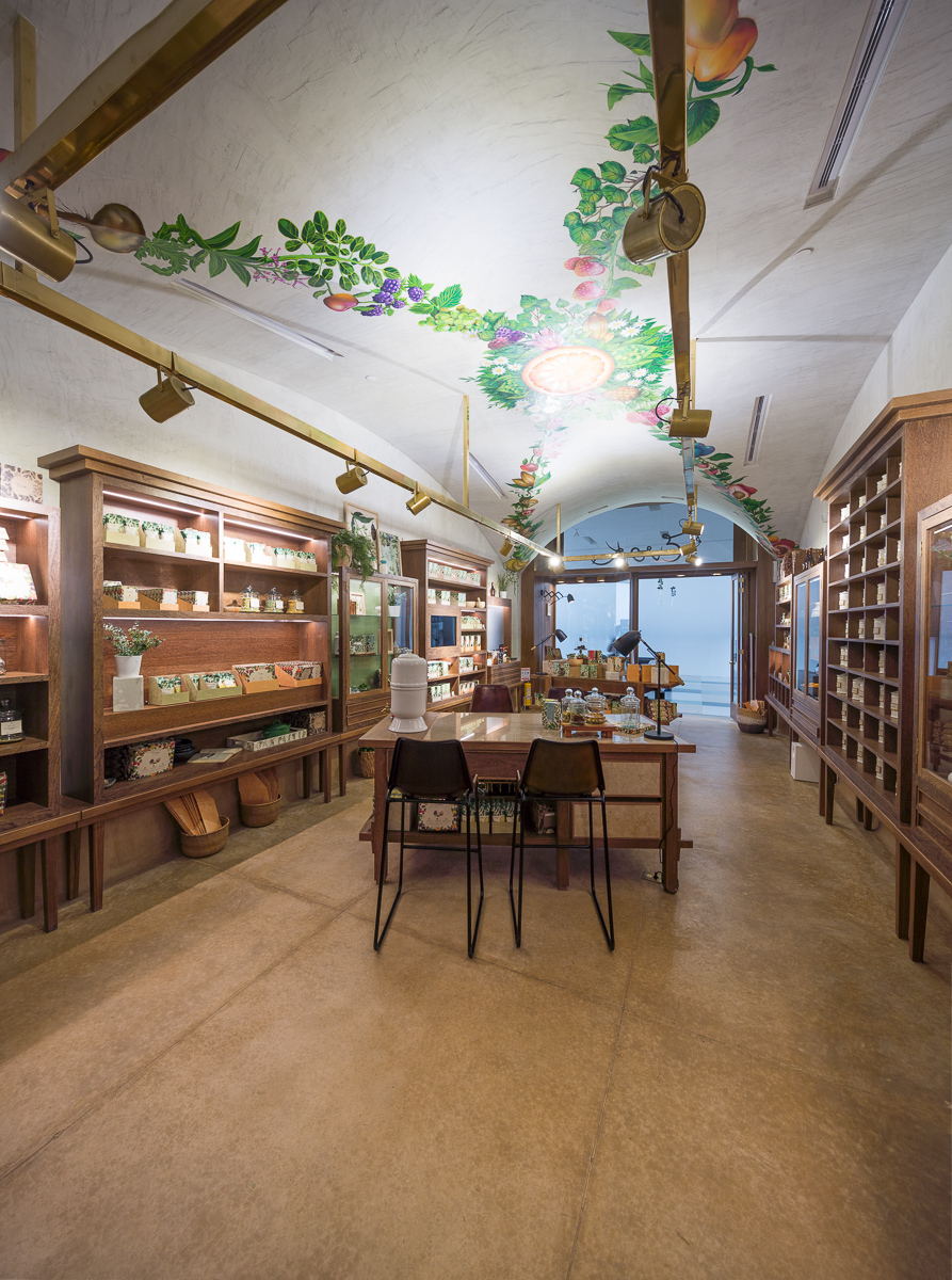 Shop interior with a vaulted ceiling painted with fruit and leaf garlands above timber shelving, a central table and brass track lights