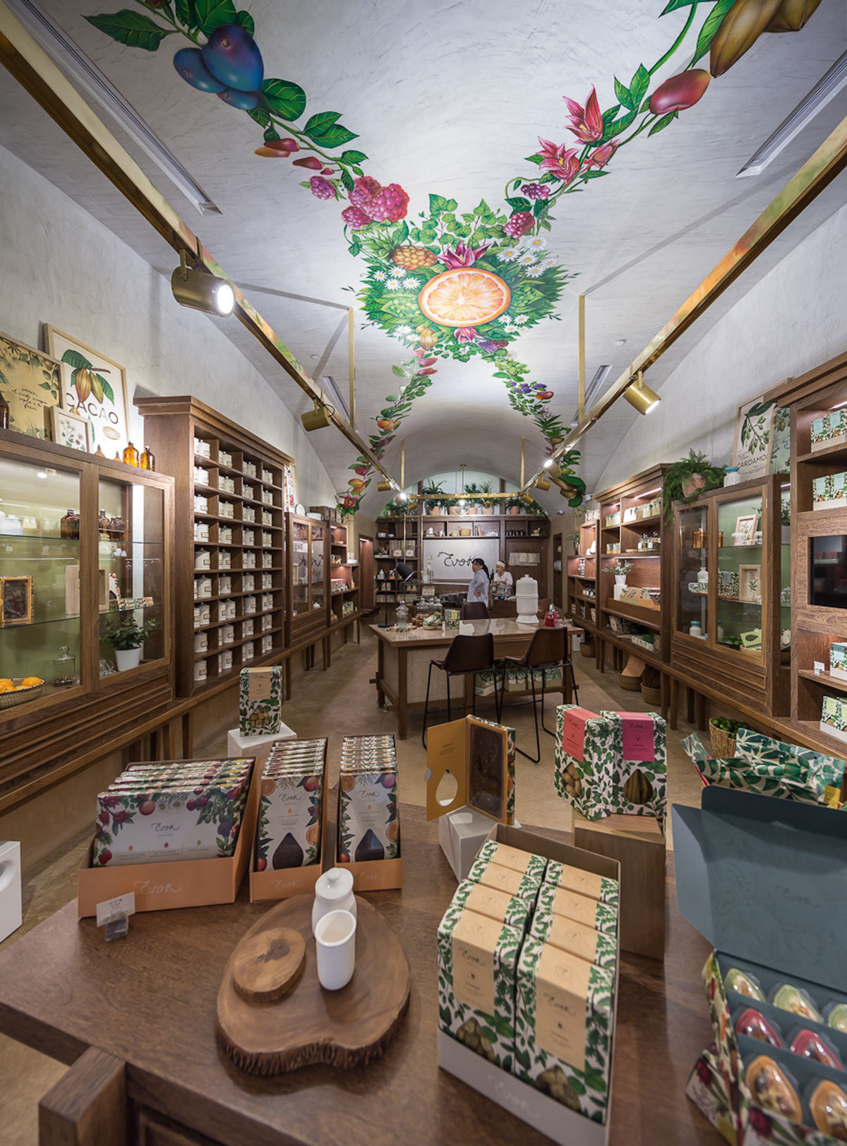 Vaulted ceiling mural of citrus and flowers seen from a product table stacked with patterned boxes of chocolate and tea