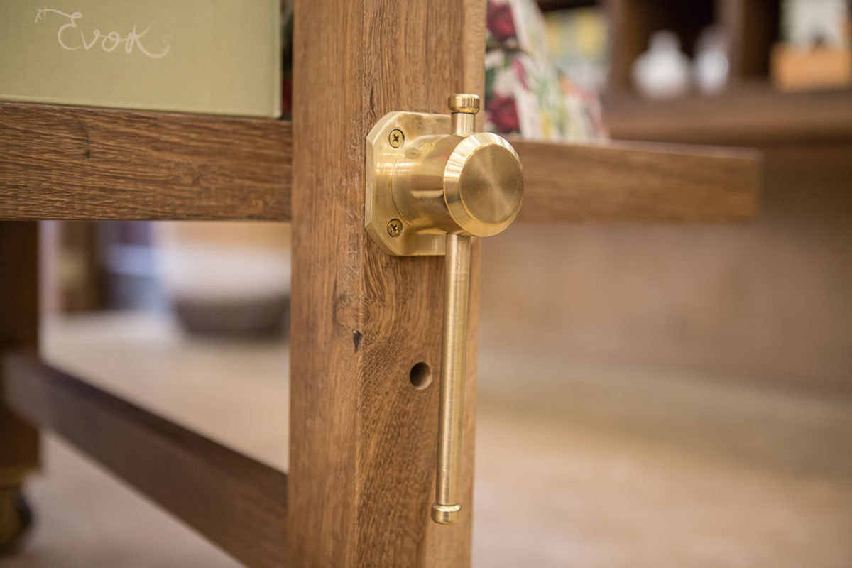 Close-up of a brass latch fixed to a solid oak frame, with shop shelving blurred behind