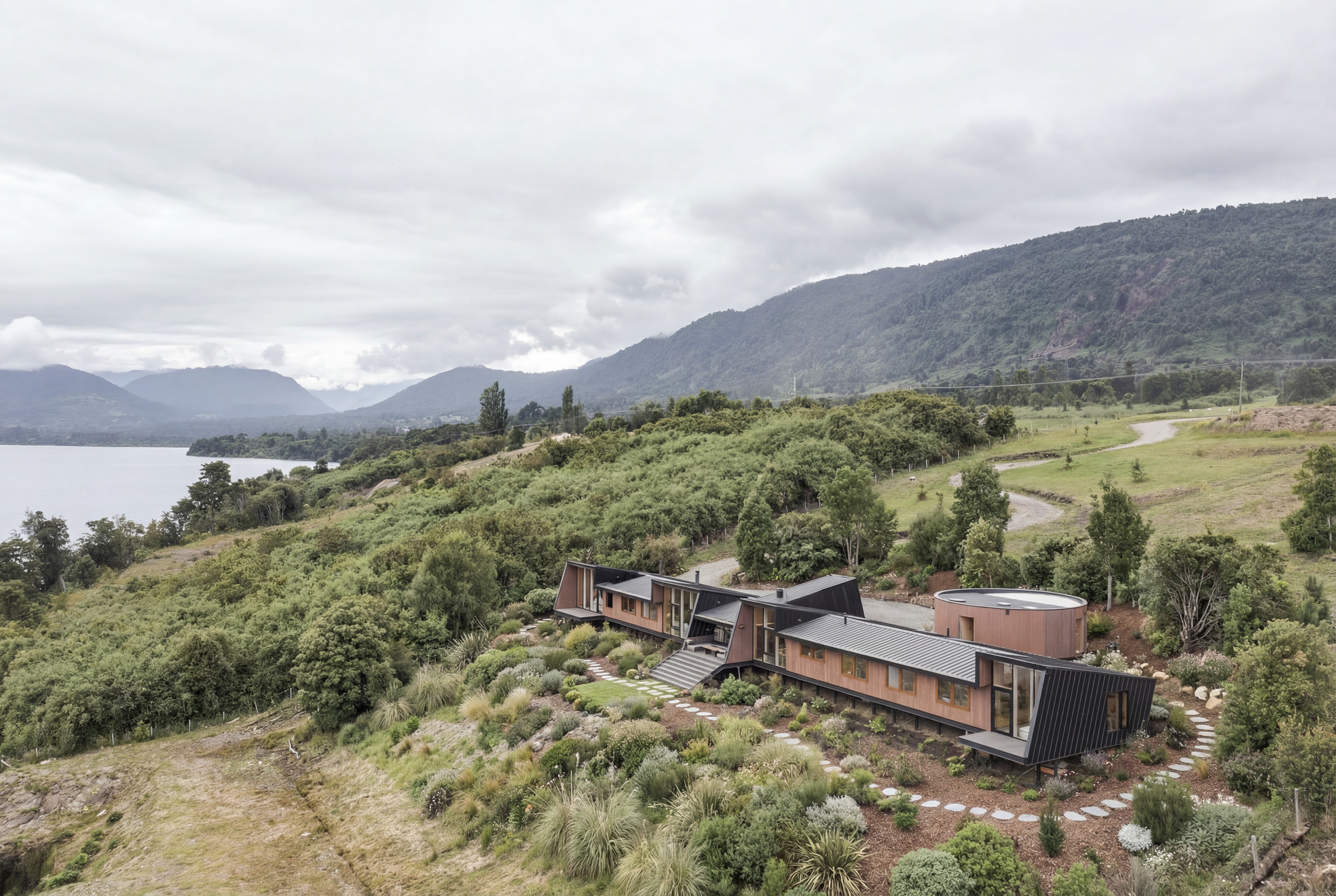 Aerial view of the compound set into a hillside planted with native vegetation overlooking a lake and distant mountains