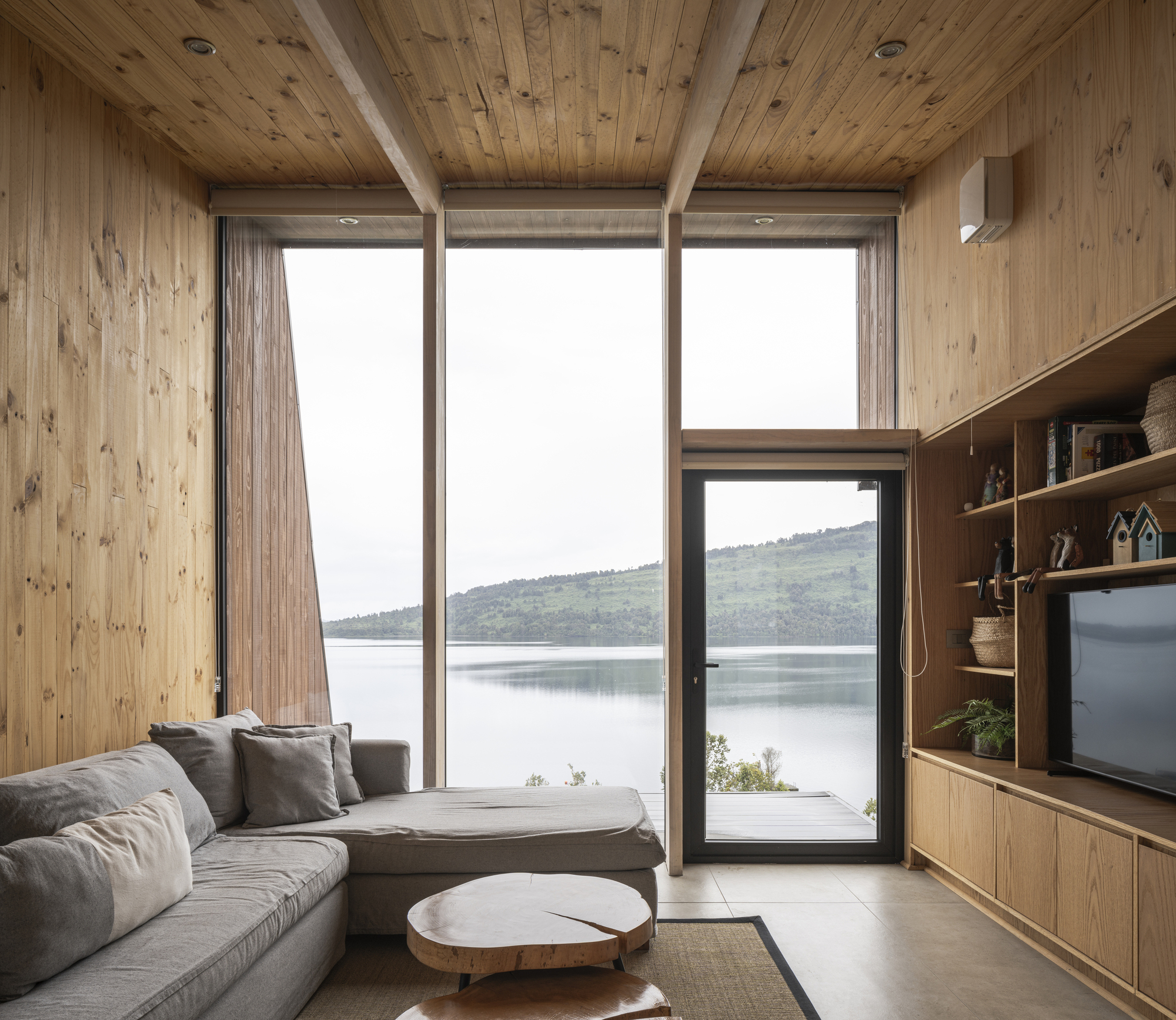 Living room with timber-clad walls and ceiling featuring floor-to-ceiling glazing framing a view across the lake to hills