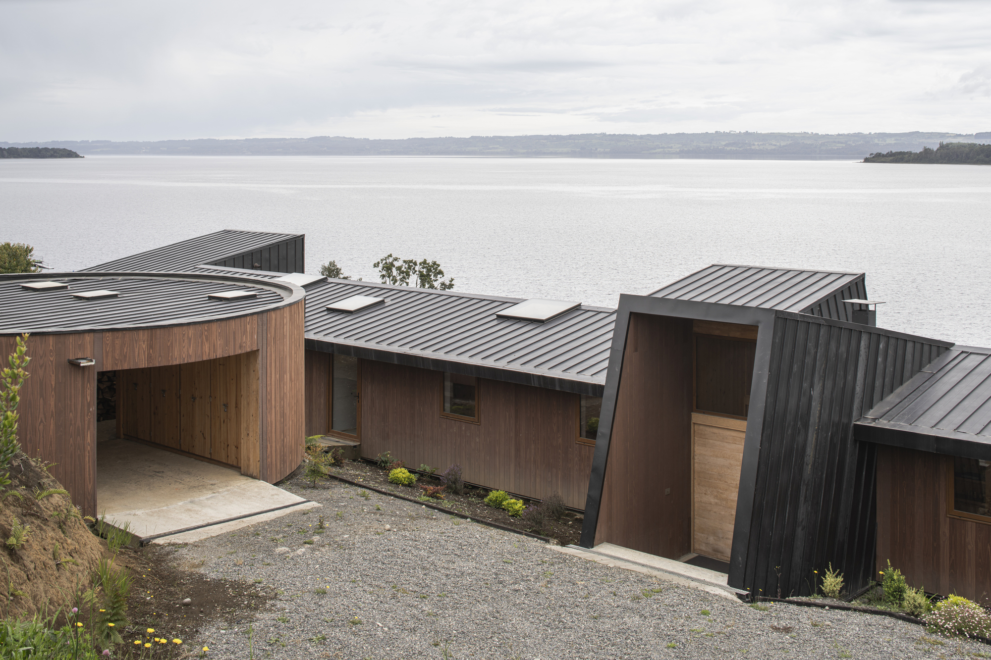 Aerial view of the clustered timber and metal roofs descending towards a calm lake shoreline
