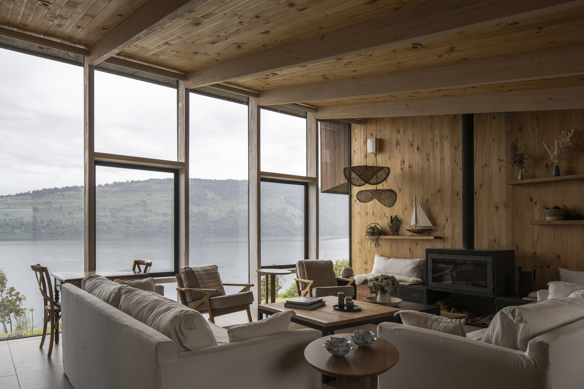 Living room with floor-to-ceiling glazing and exposed timber ceiling overlooking a misty lake