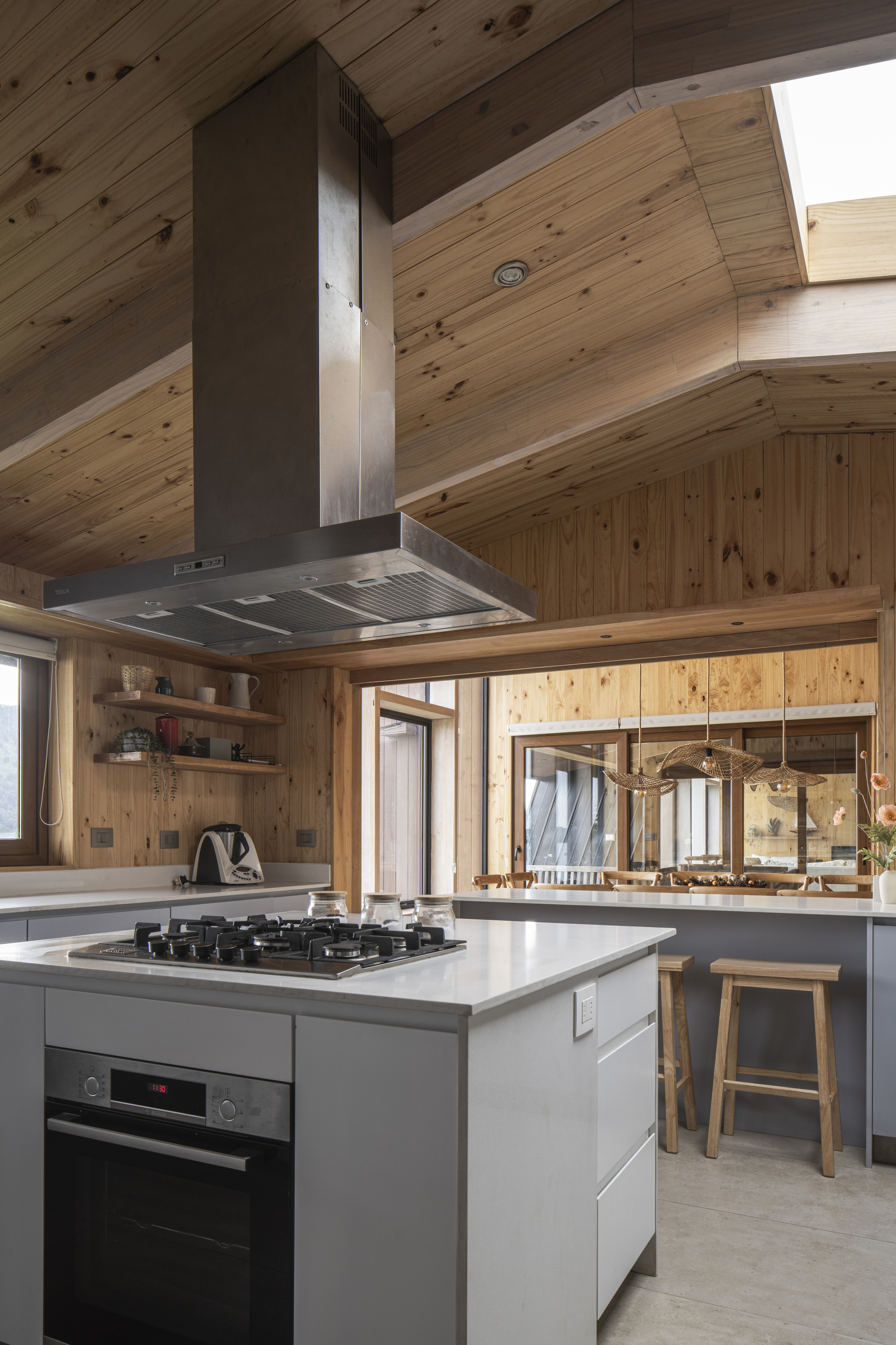 Kitchen island with suspended steel hood beneath angled timber ceiling and glazed internal partitions