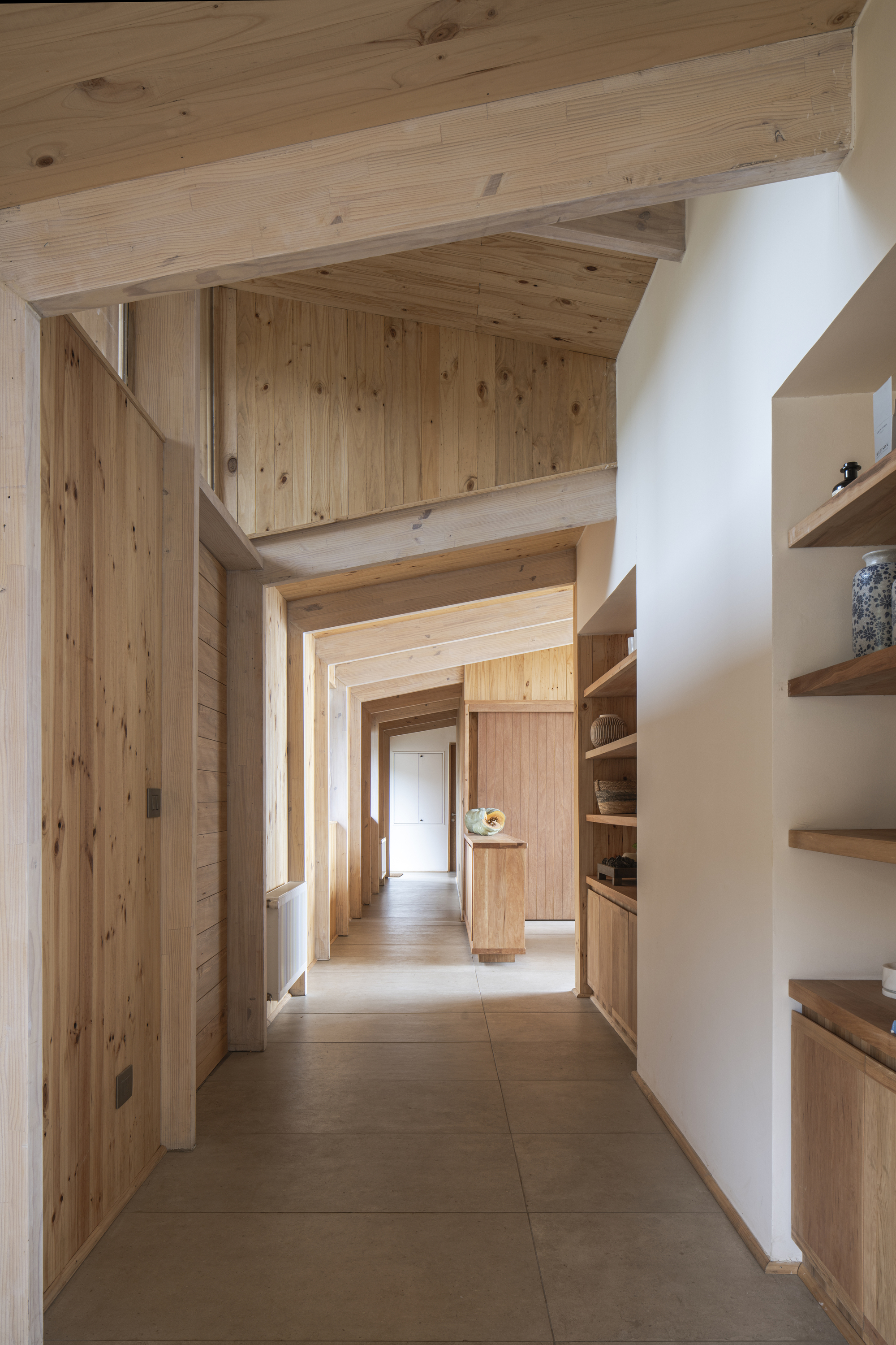 Corridor with exposed timber beams and shelving recessed into white plaster walls