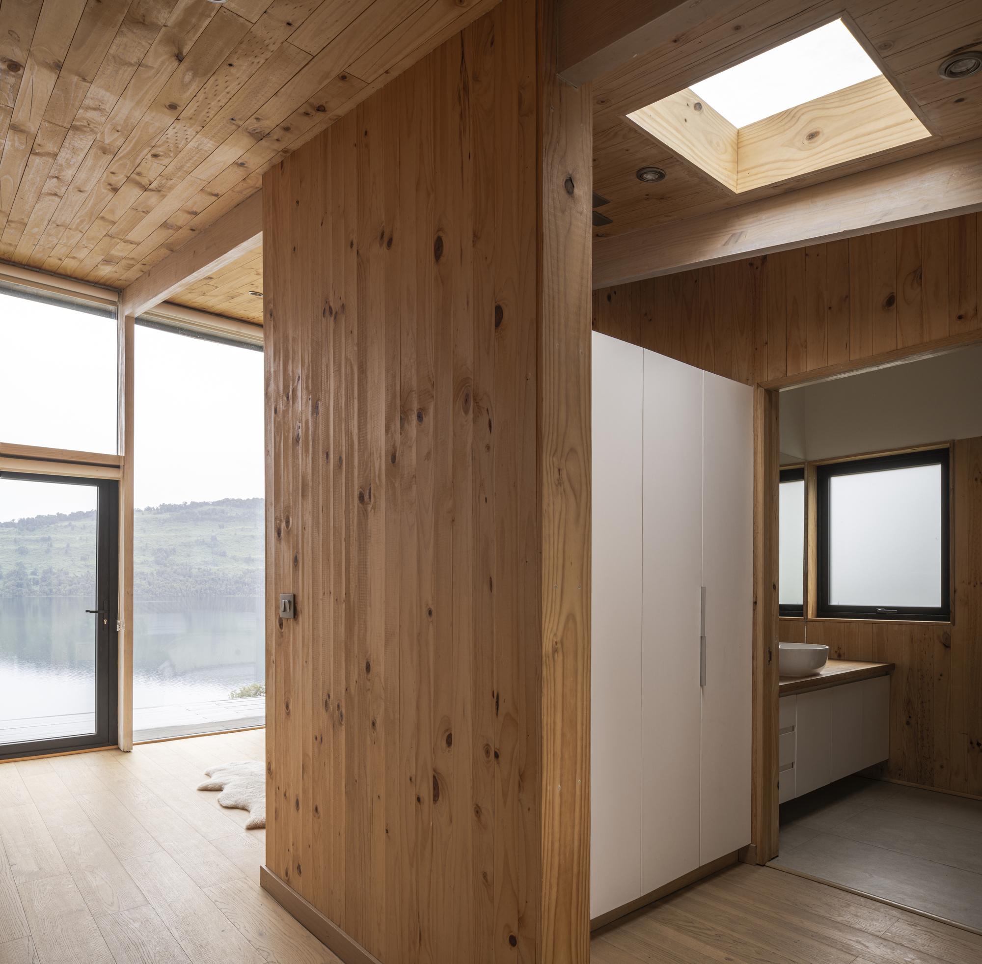 Bedroom entry with tall timber wardrobes beneath a square skylight and view to the lake