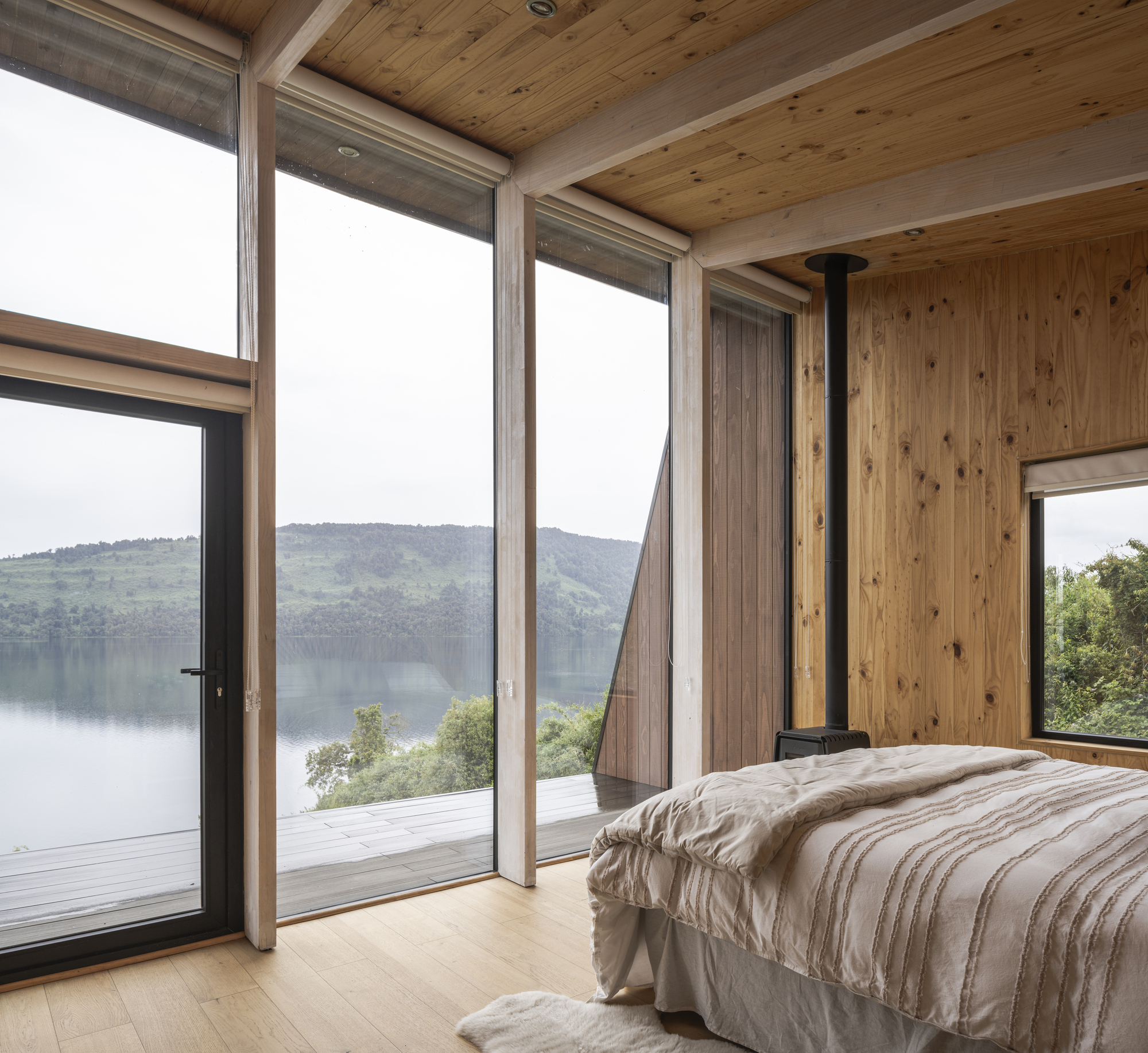 Bedroom with full-height glazing and black flue pipe framing views across the water