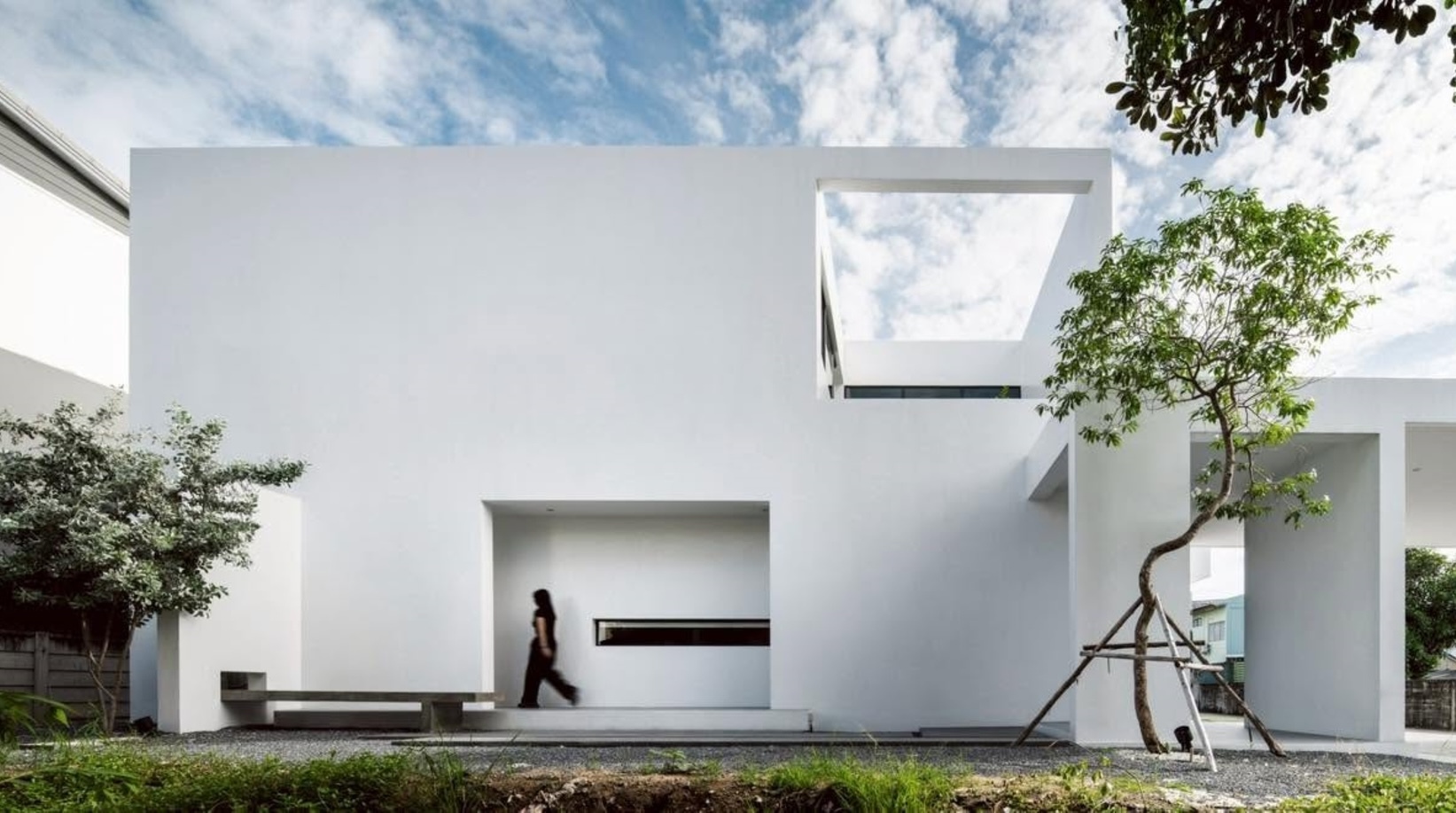 White stucco facade with rectangular voids and recessed entry as a figure walks through the courtyard