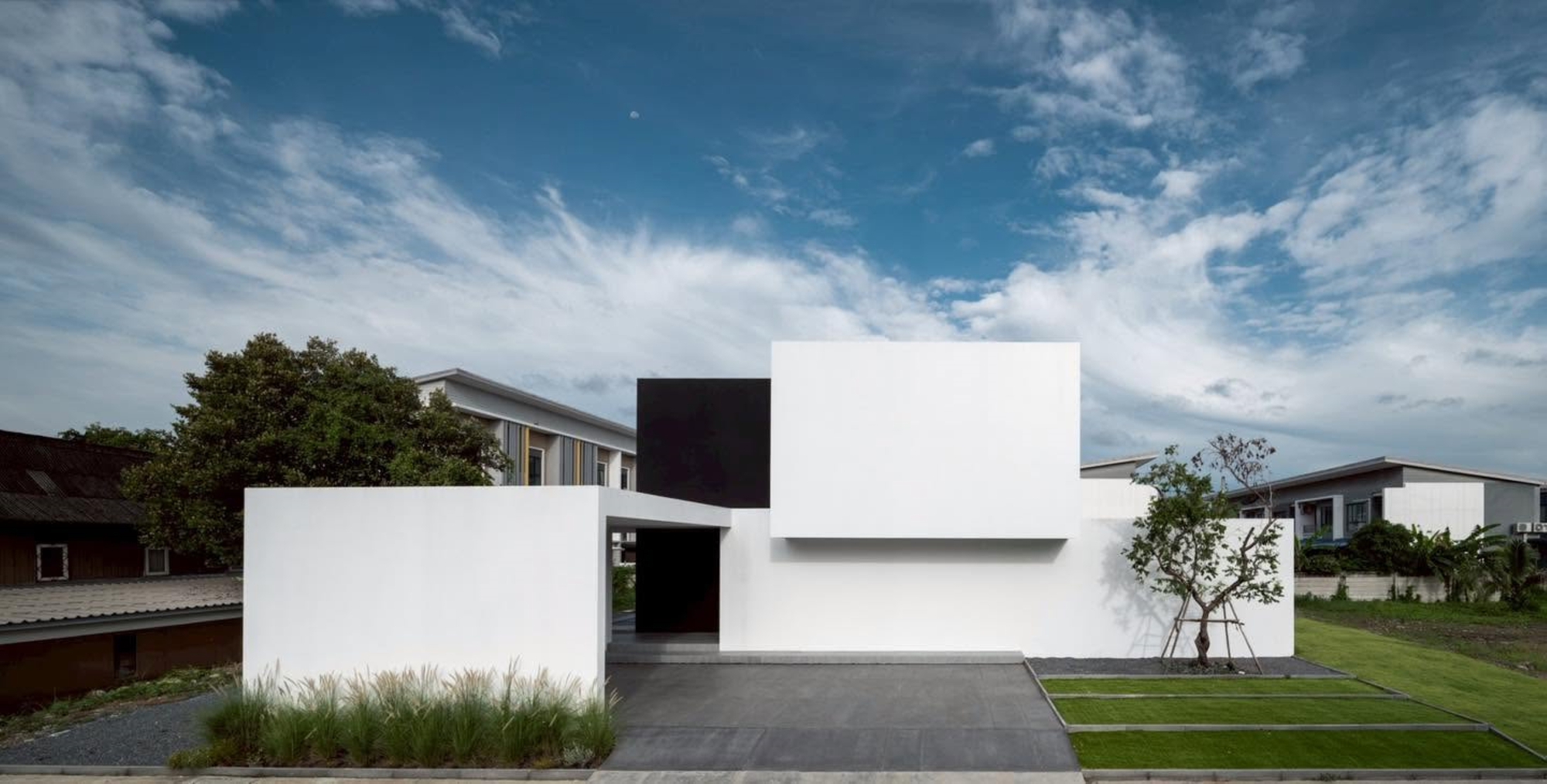 Street view of white geometric volumes with a black cantilevered box and covered entry
