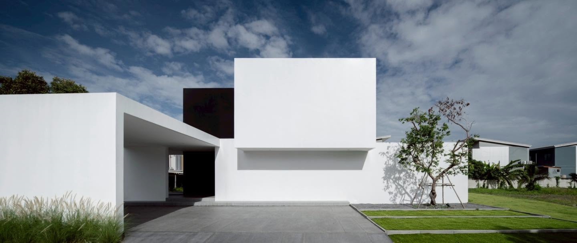 Street view of the white stucco volumes with cantilever and recessed entry under scattered clouds