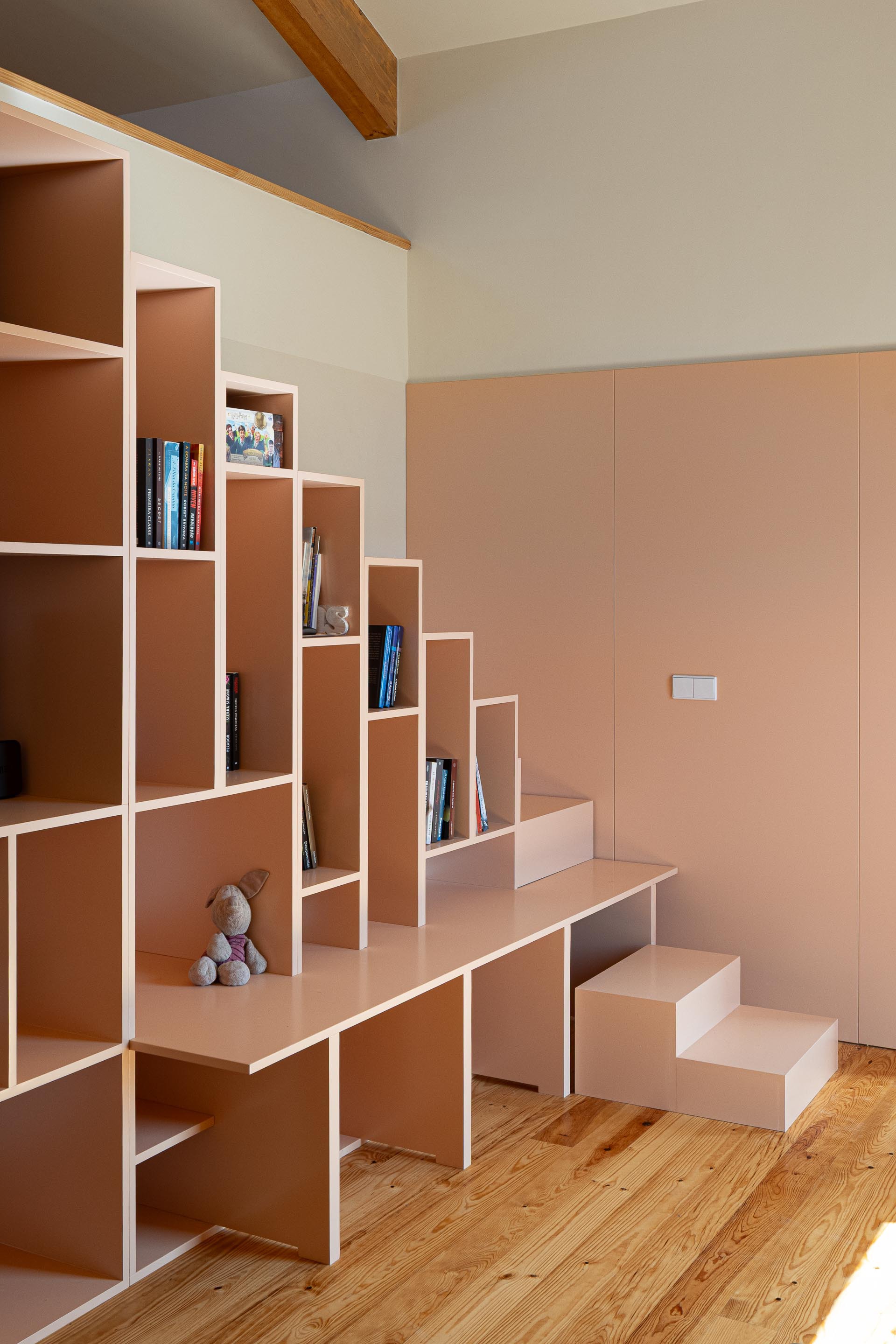 Integrated staircase and shelving unit in pink with stepped geometric compartments on timber flooring