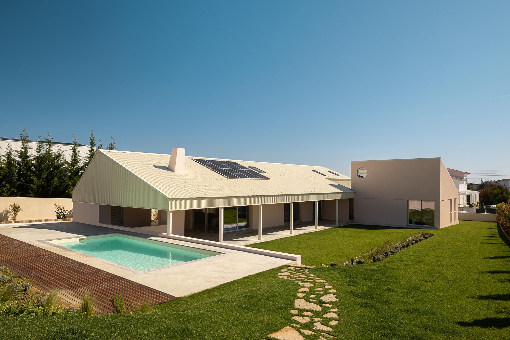 Rear facade with corrugated metal gable roof, solar panels, pool, and stepping stone path through lawn