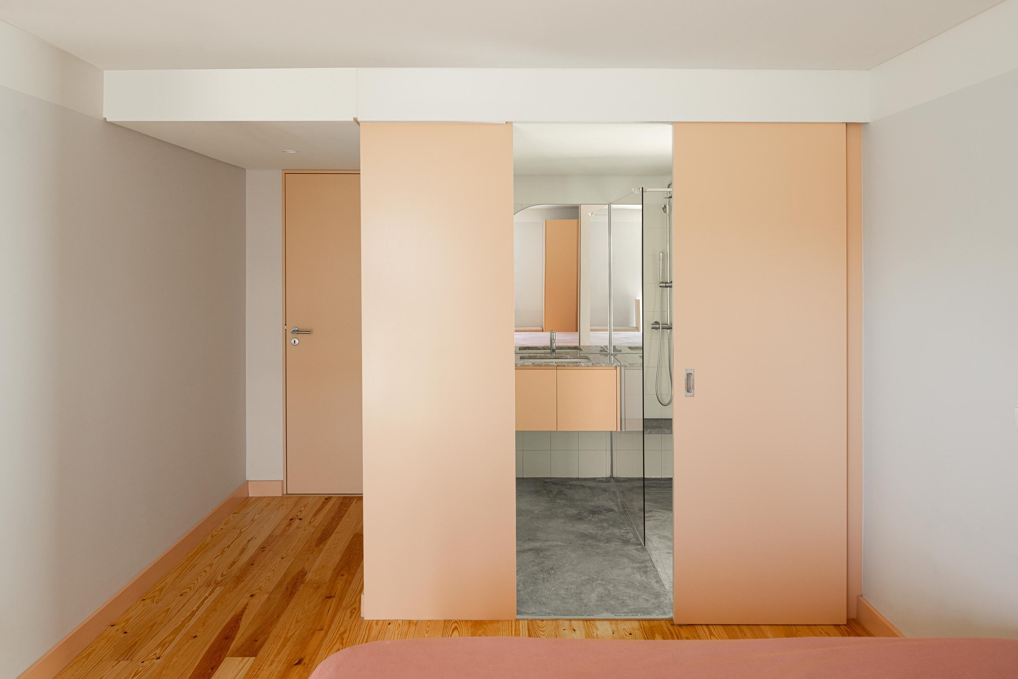 View through pink sliding panels into bathroom with glass shower enclosure and concrete floor