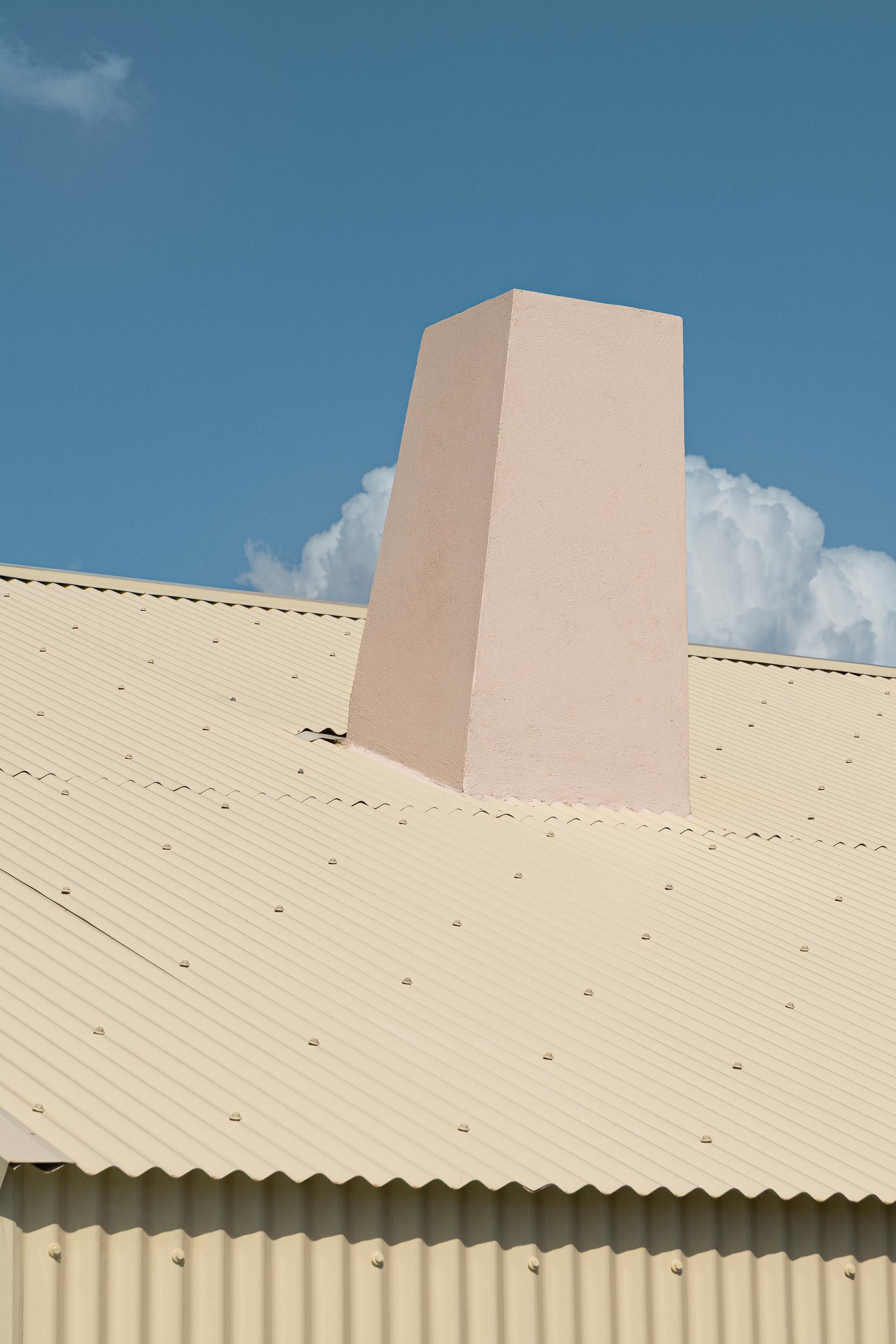 Tapered pink stucco chimney rising from a corrugated metal roof against white clouds