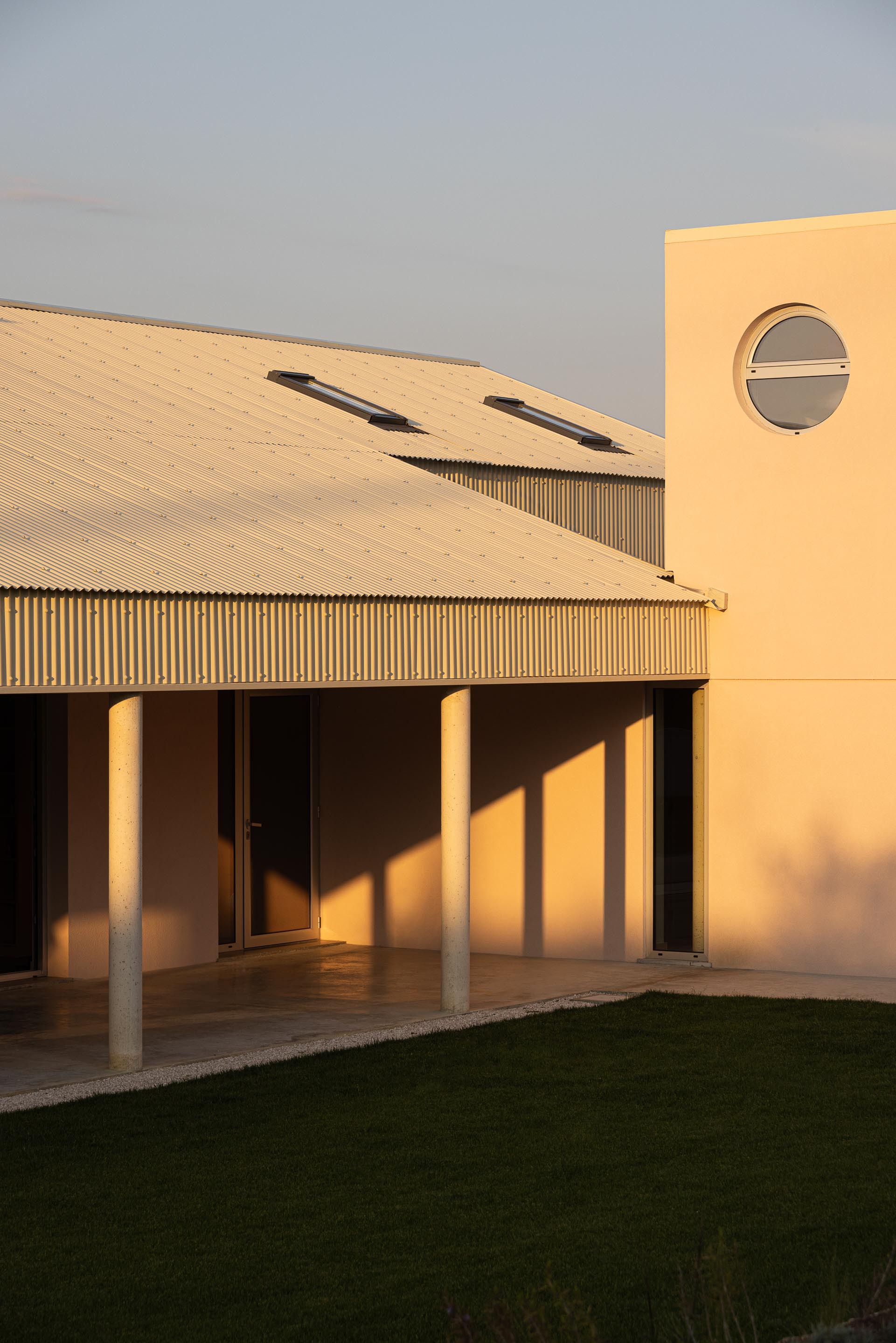 Covered terrace with column shadows stretching across floor at sunset beside circular window