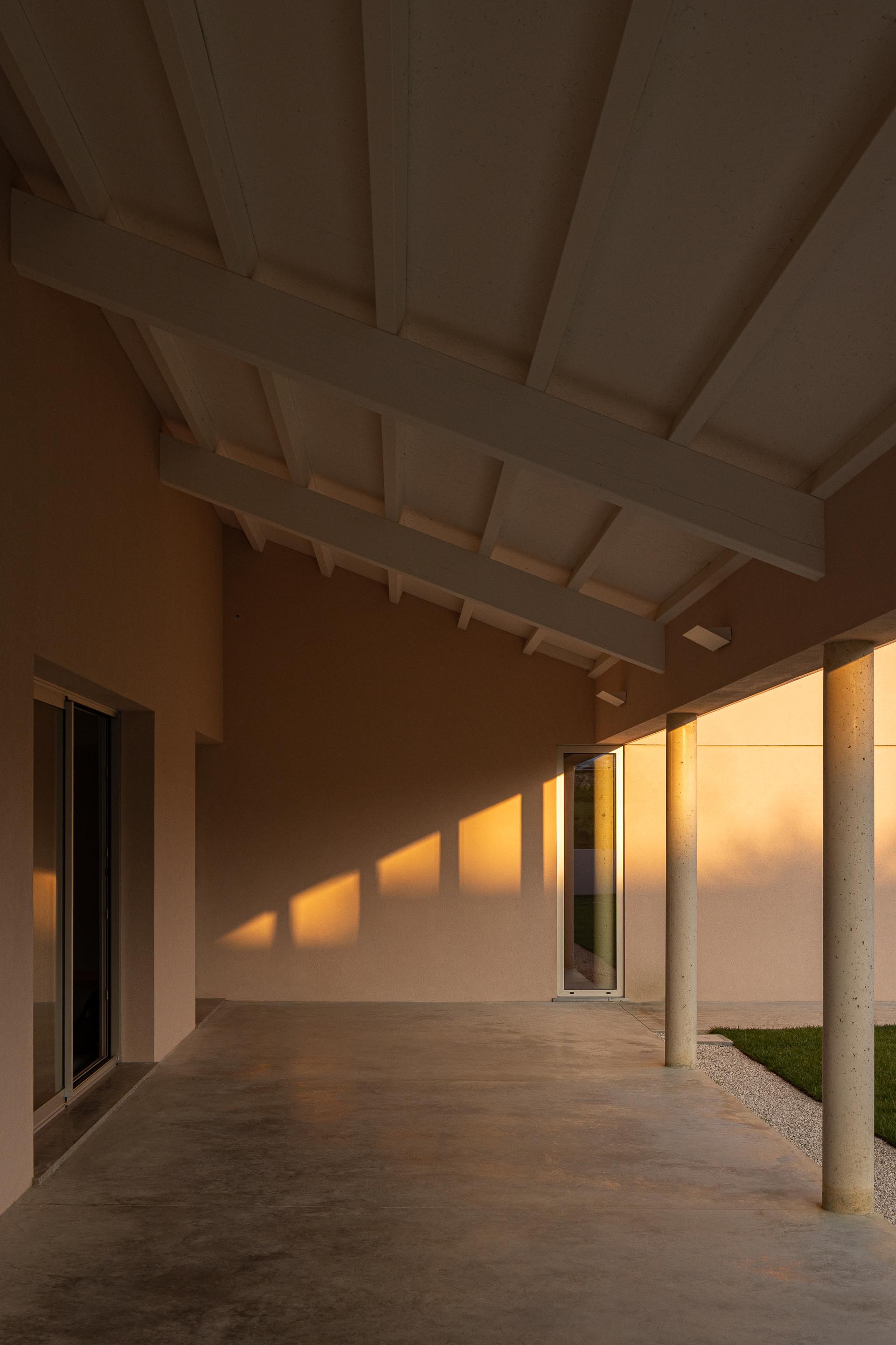 Covered walkway with exposed timber rafters and concrete columns casting long shadows in afternoon light