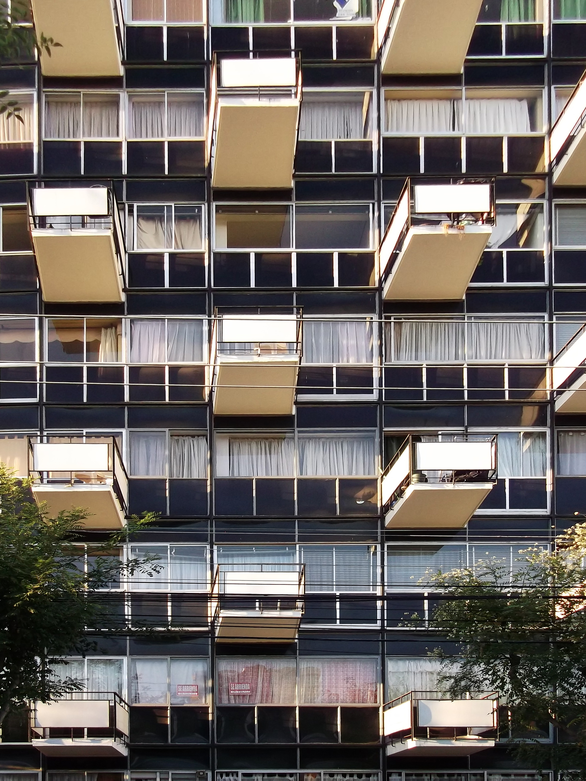Facade detail of the glass and metal balcony grid with projecting tan panels in afternoon light