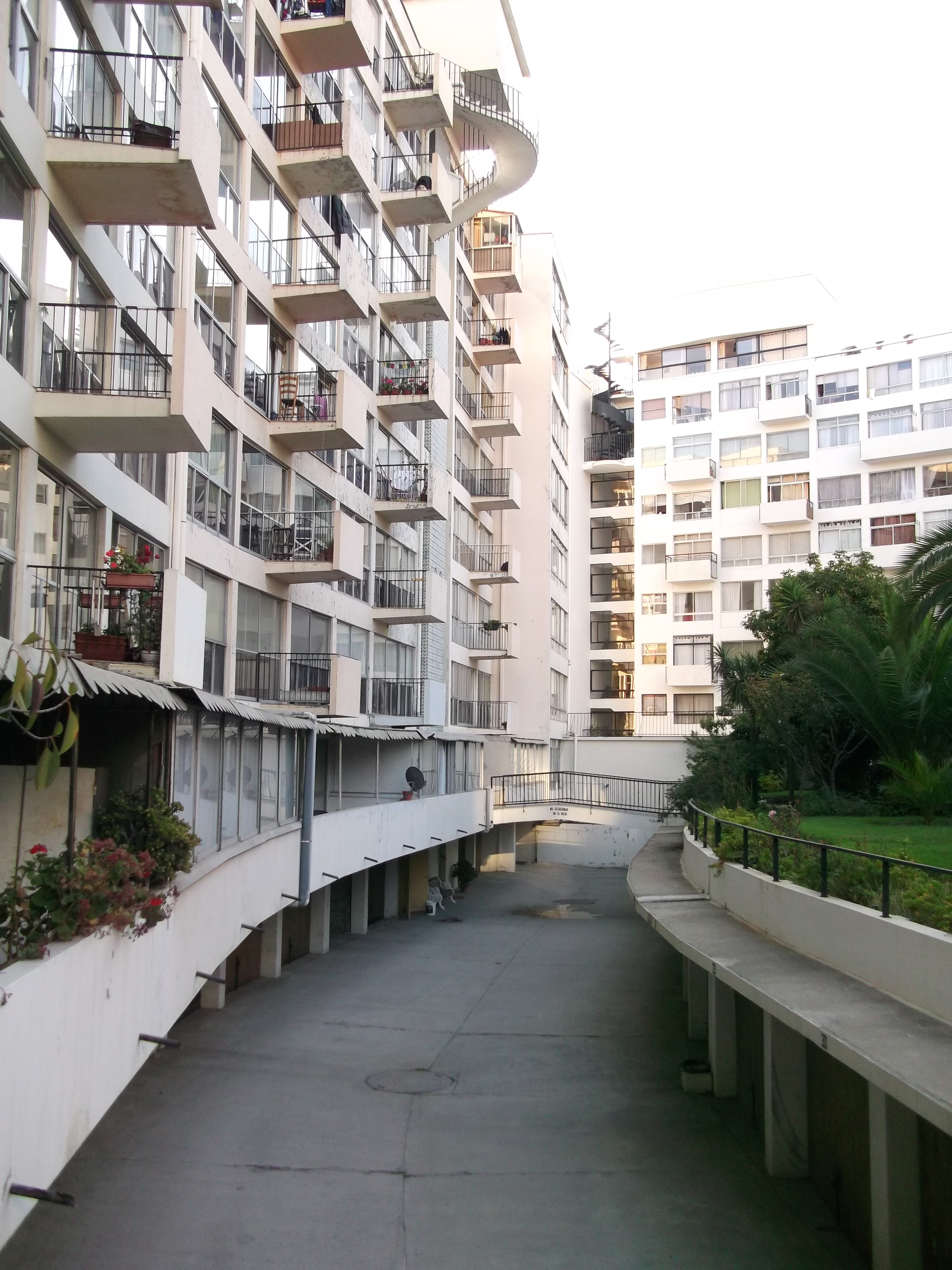 Curved pedestrian ramp between residential towers with a person walking in the distance at dusk