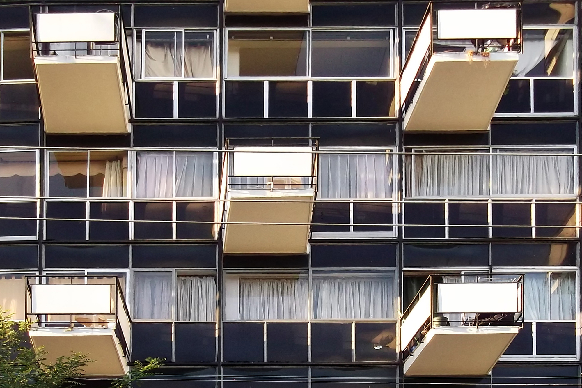 Close-up of the balcony facade showing alternating glass panels and tan balcony screens with metal railings