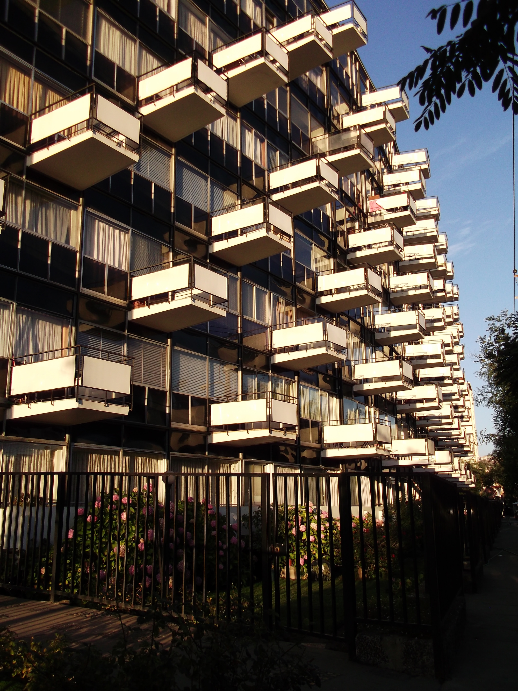 Facade detail of the interlocking concrete balconies in warm afternoon light behind a planted fence