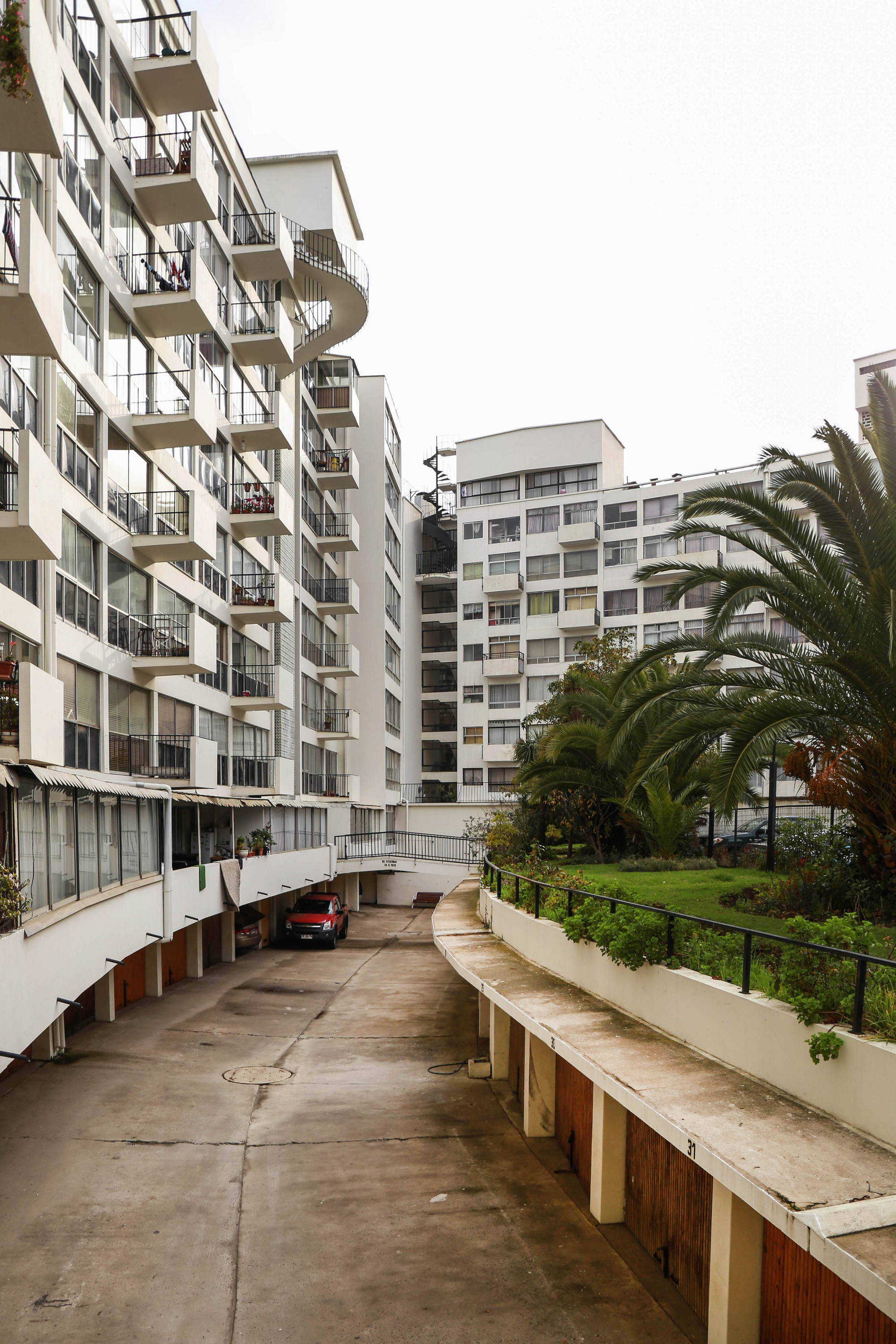 Ground level driveway ramp leading beneath the residential blocks with palm trees and lawn on overcast day