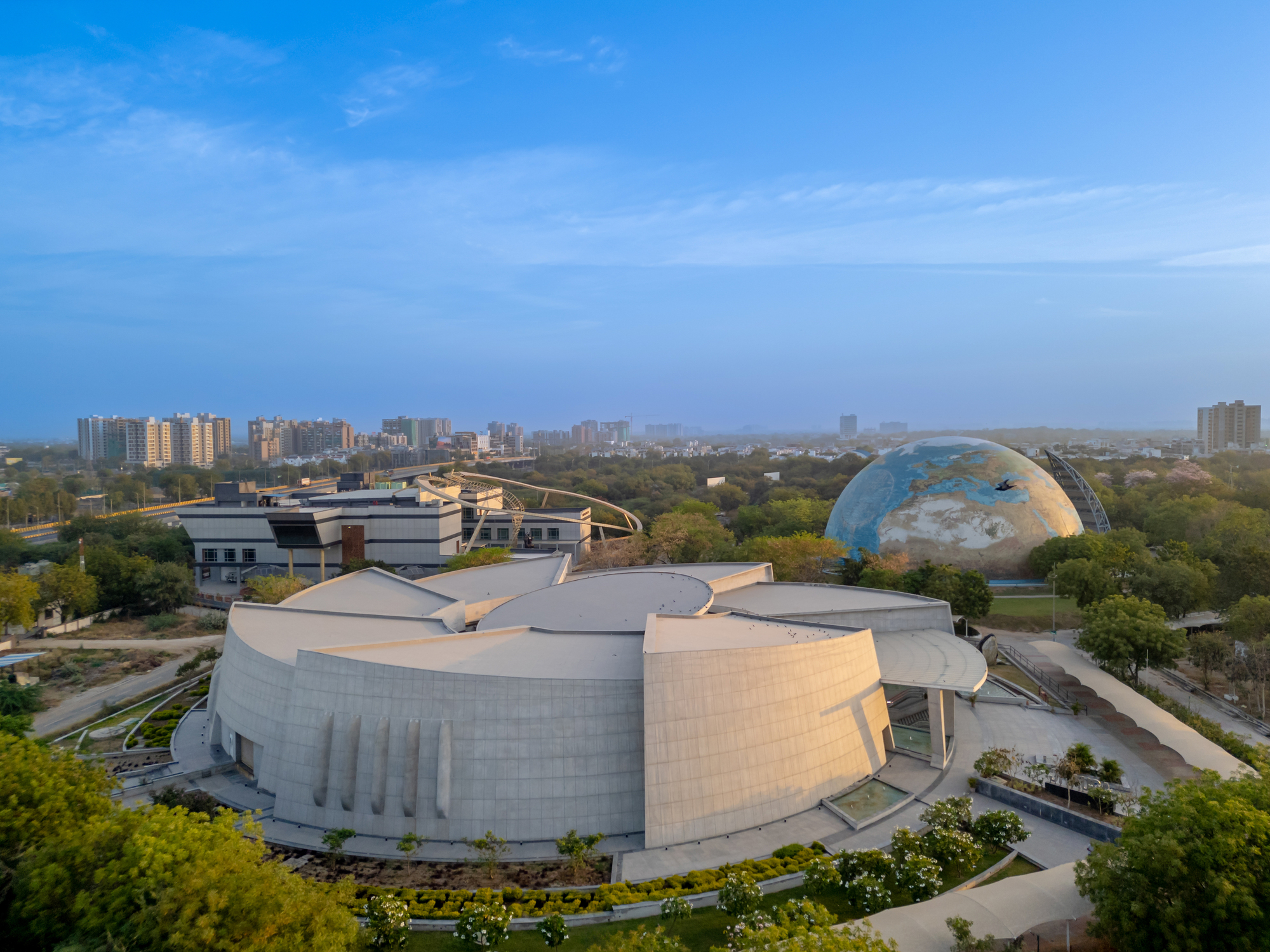 Aerial view of the curved petal-shaped roof volumes surrounding a central cylindrical dome with dome structure in background