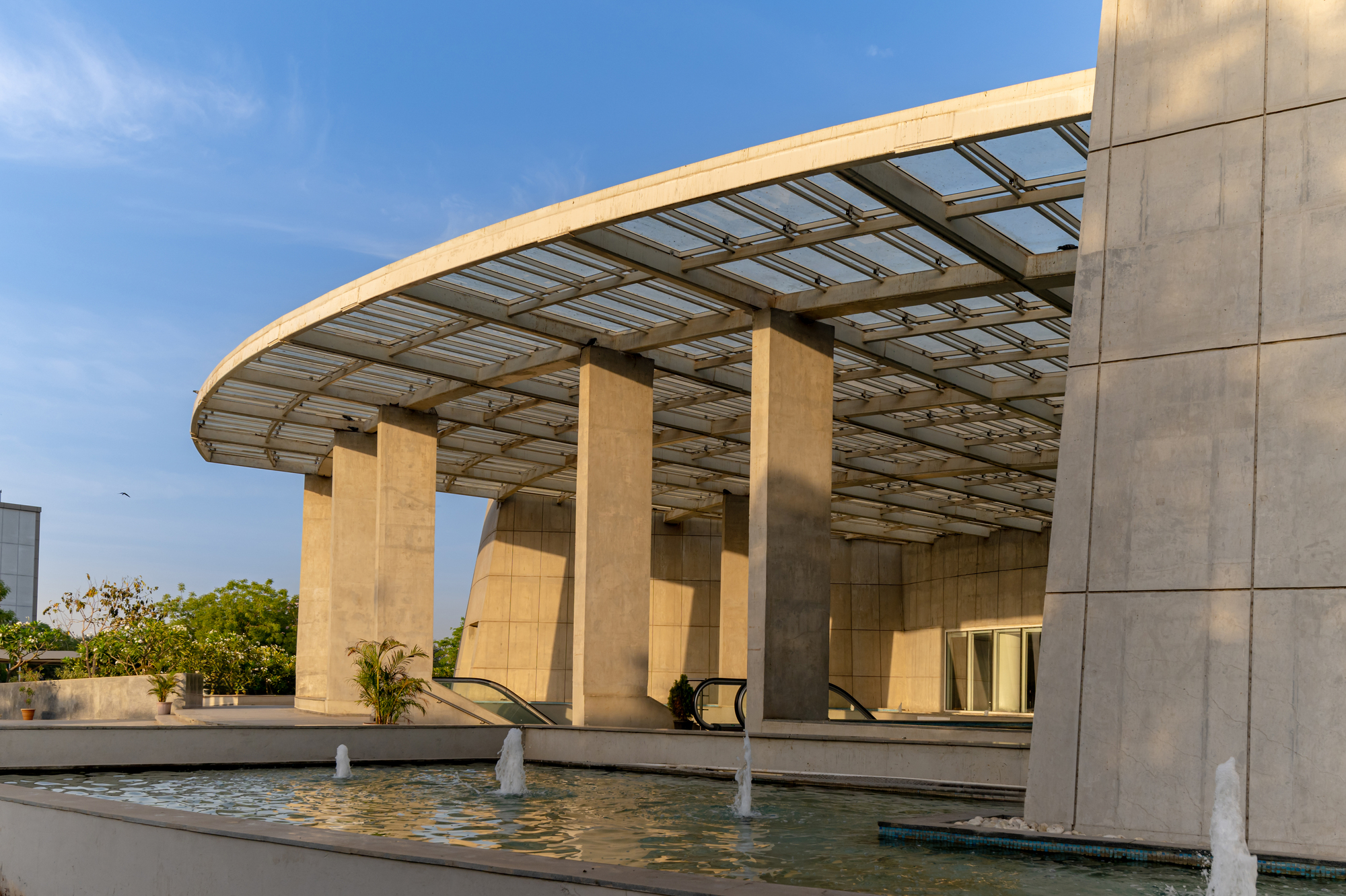 Covered entrance portico with stone piers supporting a glazed canopy over a reflecting pool with fountains