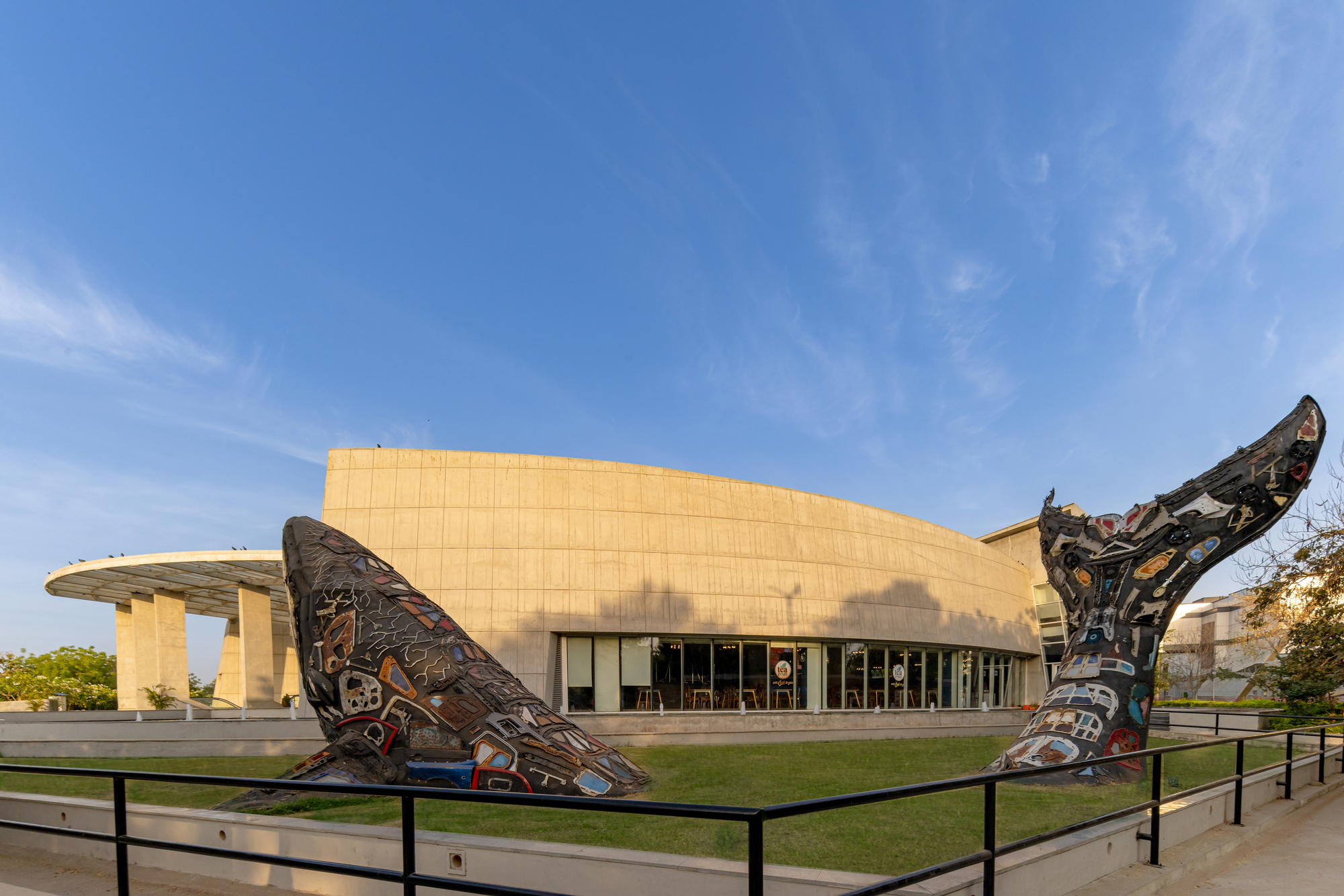 Curved beige stone facade with glazed entrance and carved sculptural totems on the lawn