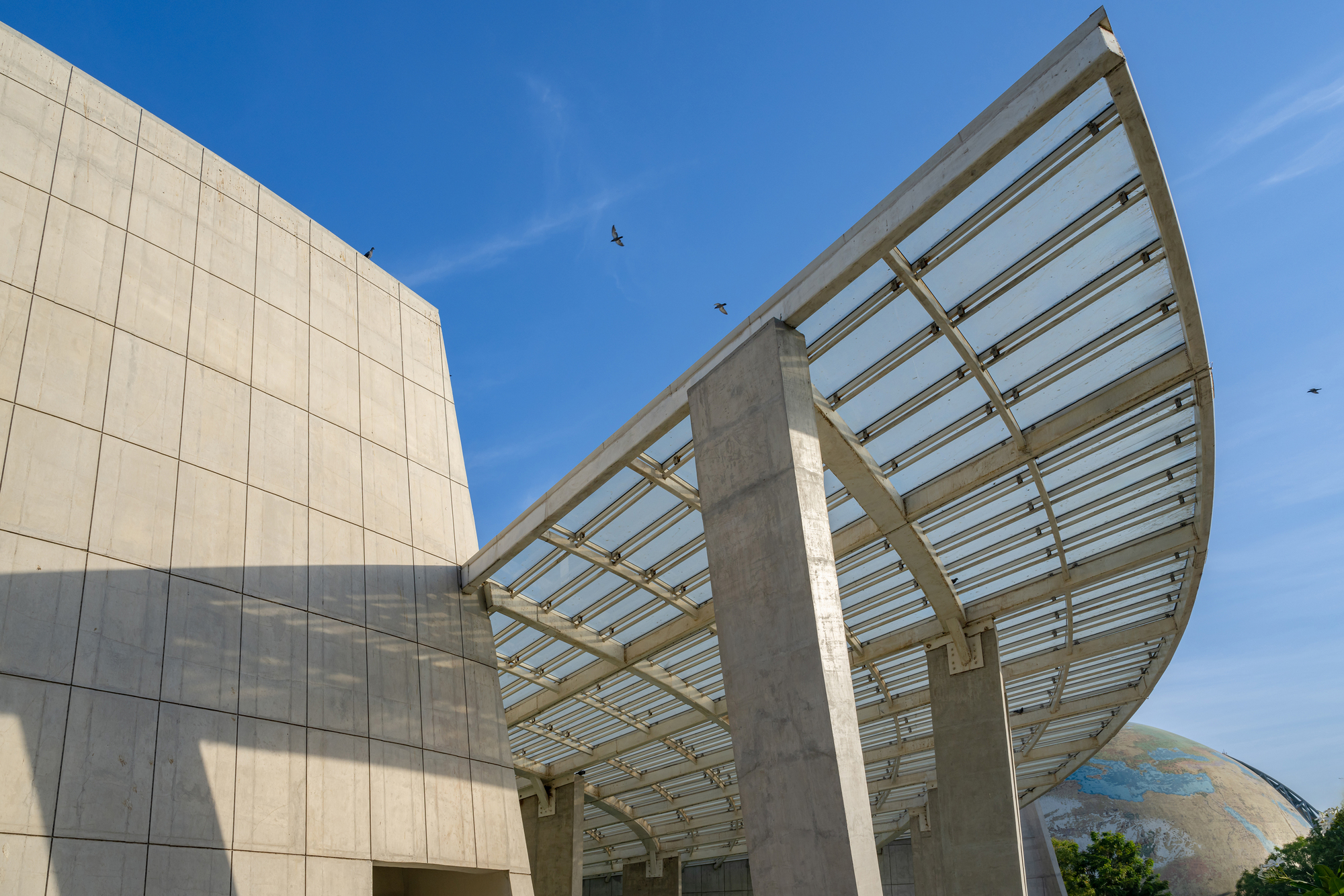 Curved canopy with exposed steel ribs and concrete columns against a clear blue sky