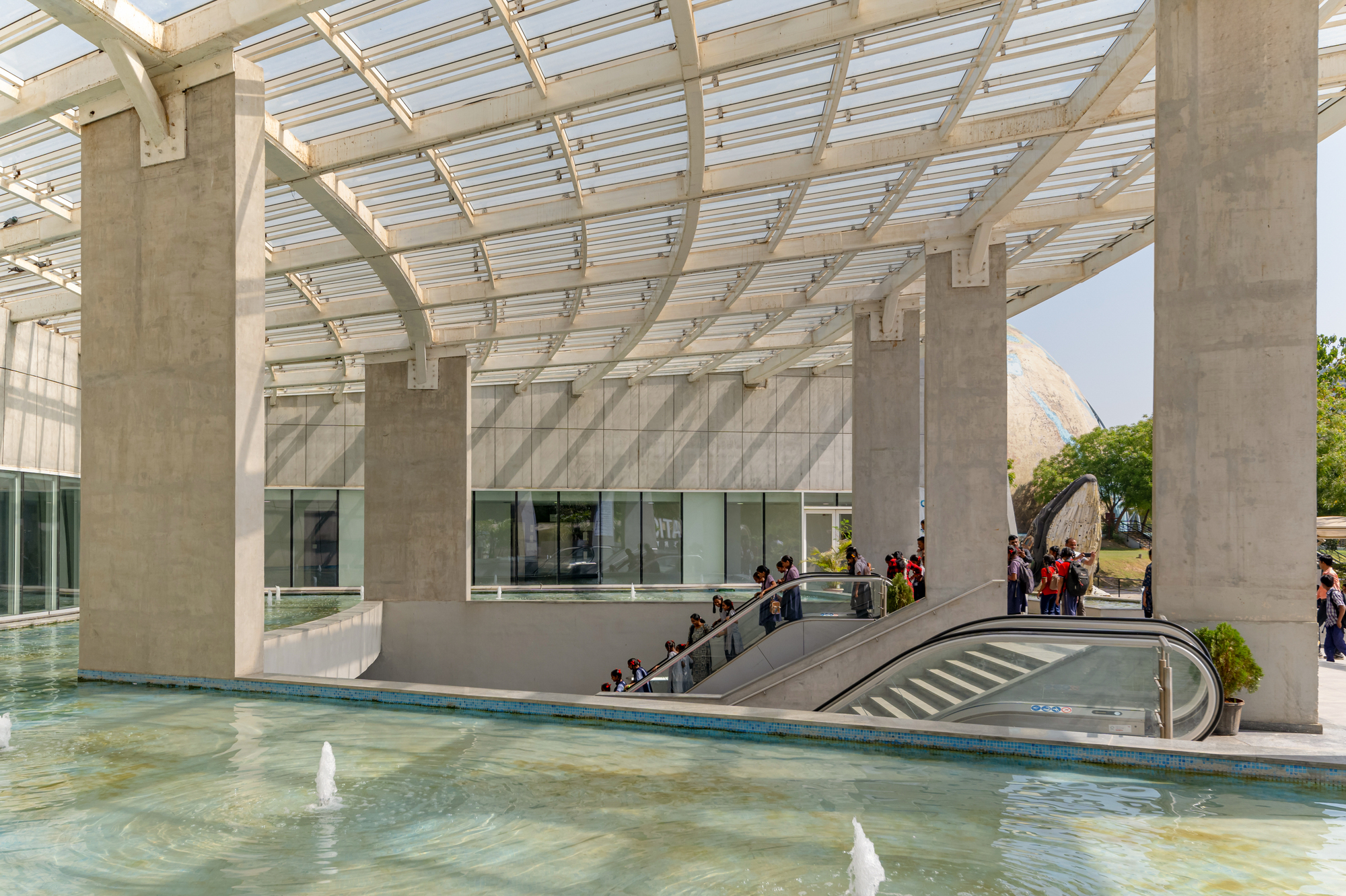 Entrance courtyard with reflecting pool, curved ramp, and glass-ribbed canopy overhead