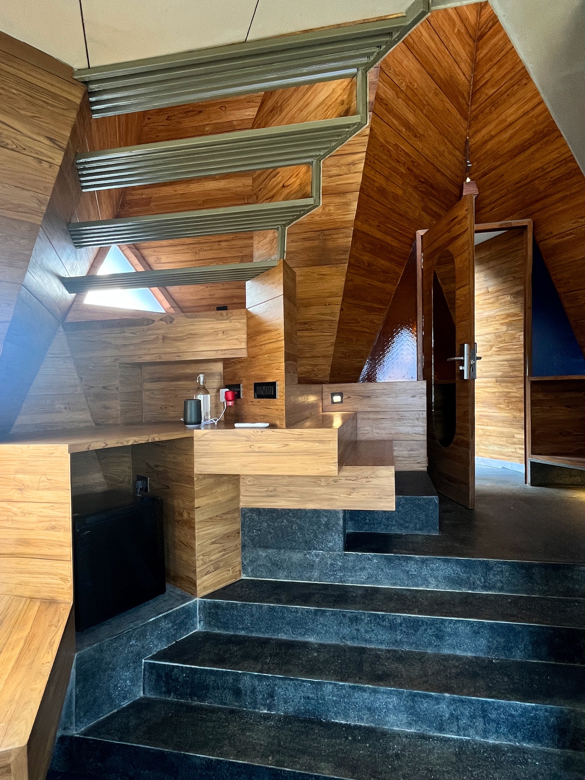 Concrete staircase ascending through an angular wood-clad interior space with skylights above