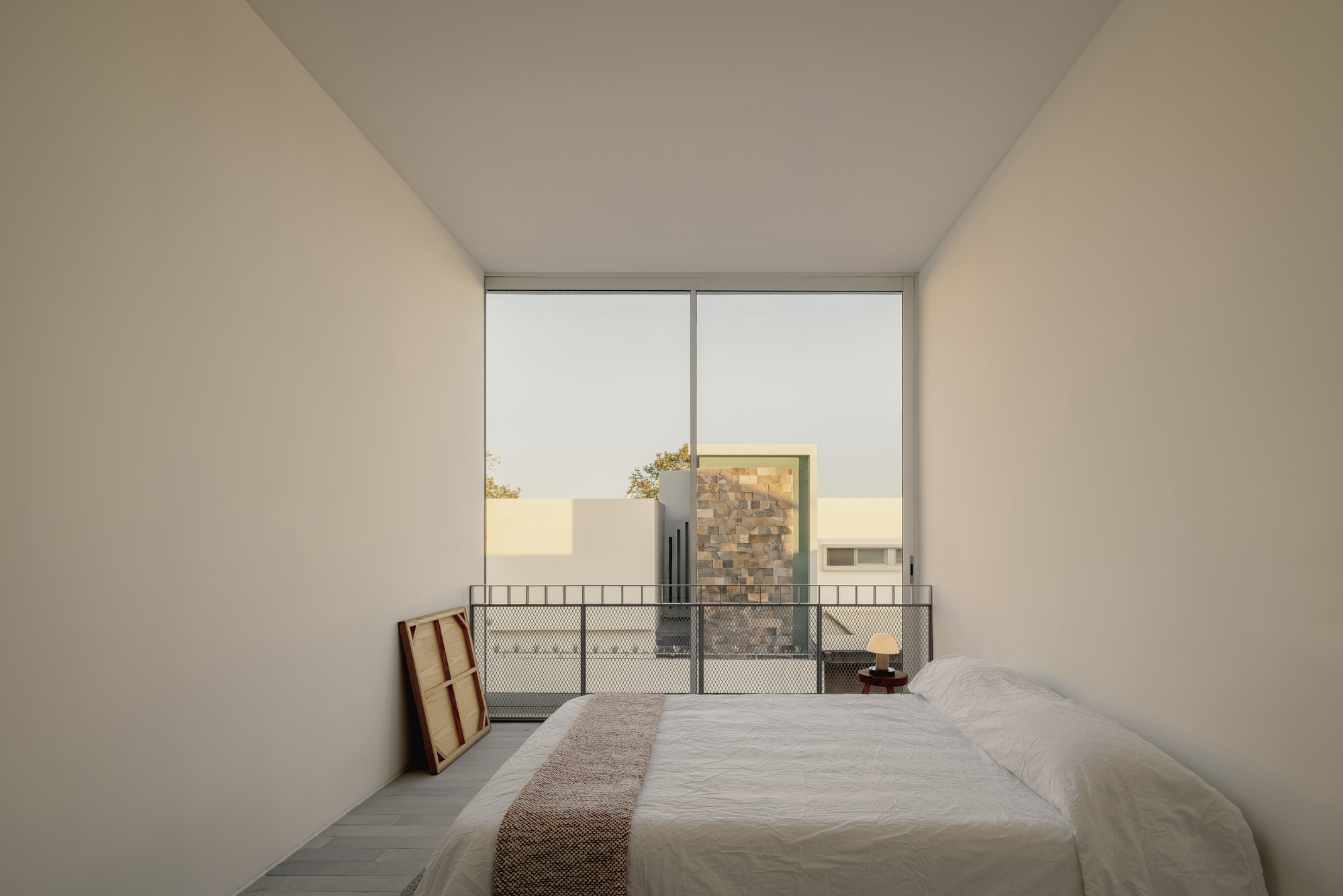 Bedroom with low platform bed facing a glazed door opening onto a courtyard at dusk