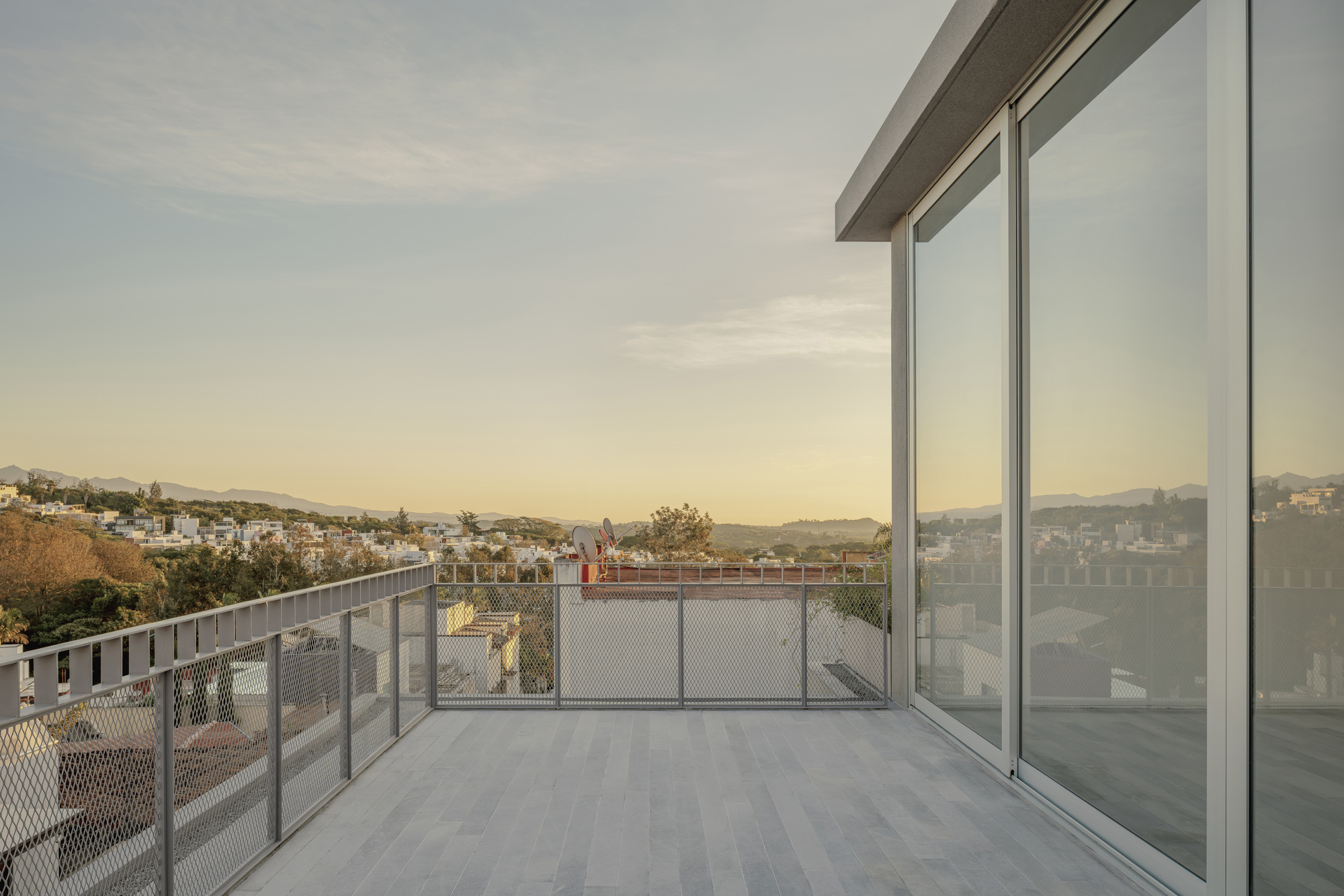 Rooftop terrace with metal mesh railing overlooking a hilly residential neighborhood at sunset