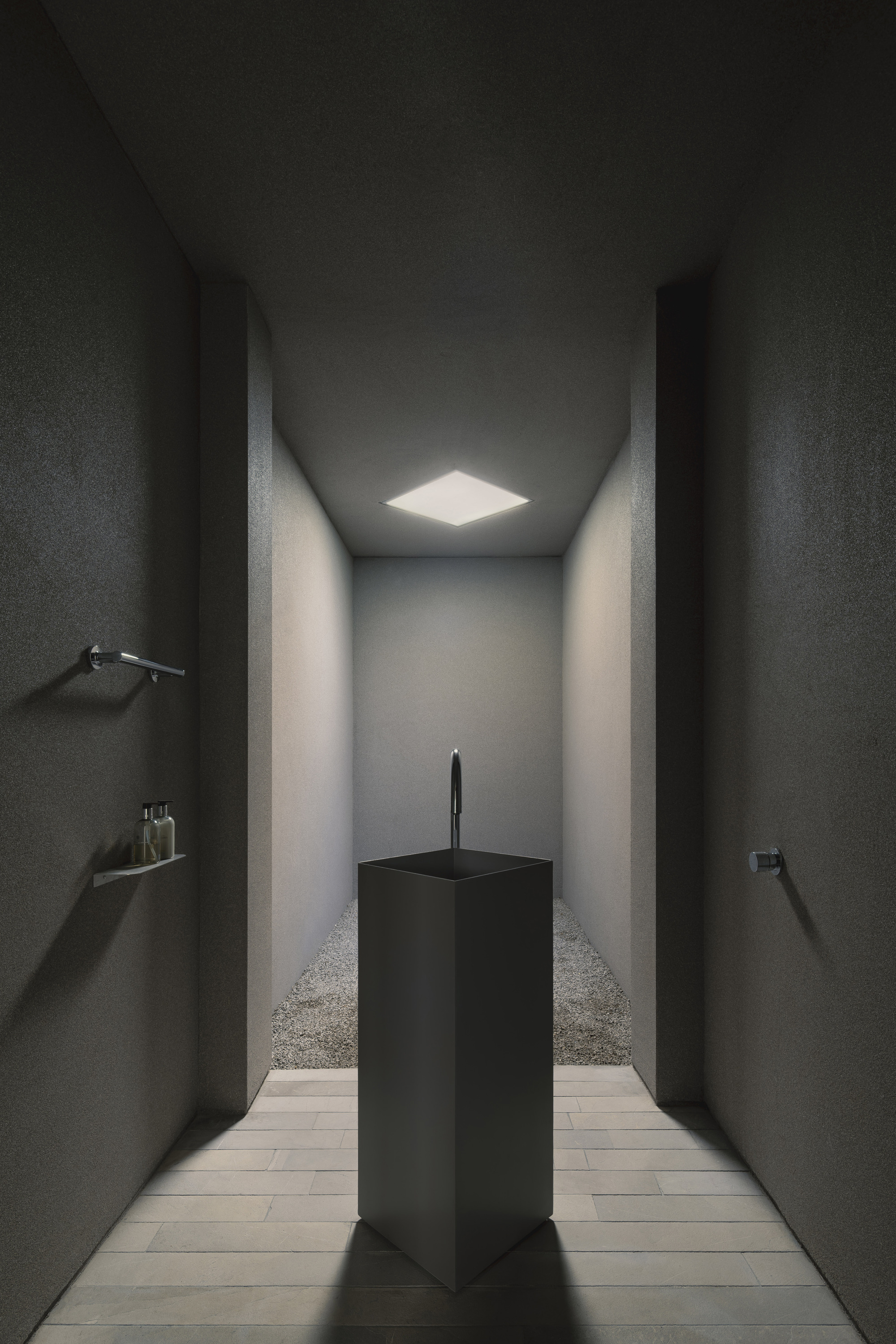 Narrow corridor with dark textured walls and a single skylight illuminating a black pedestal sink