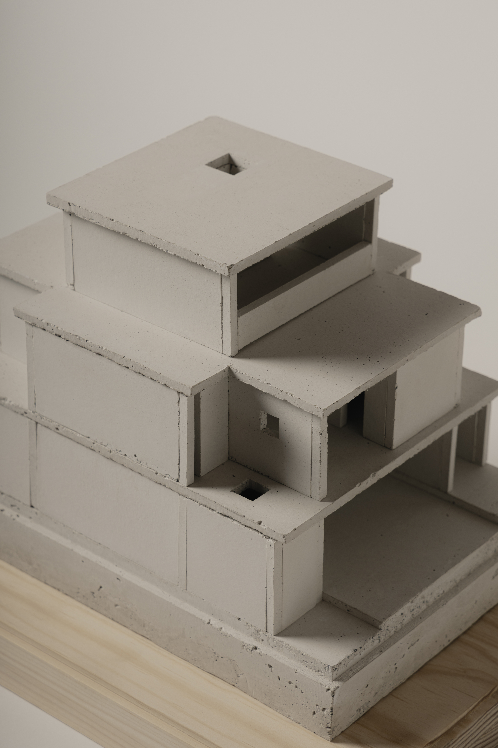 Close-up of a concrete study model with stacked volumes and open voids on a plywood base