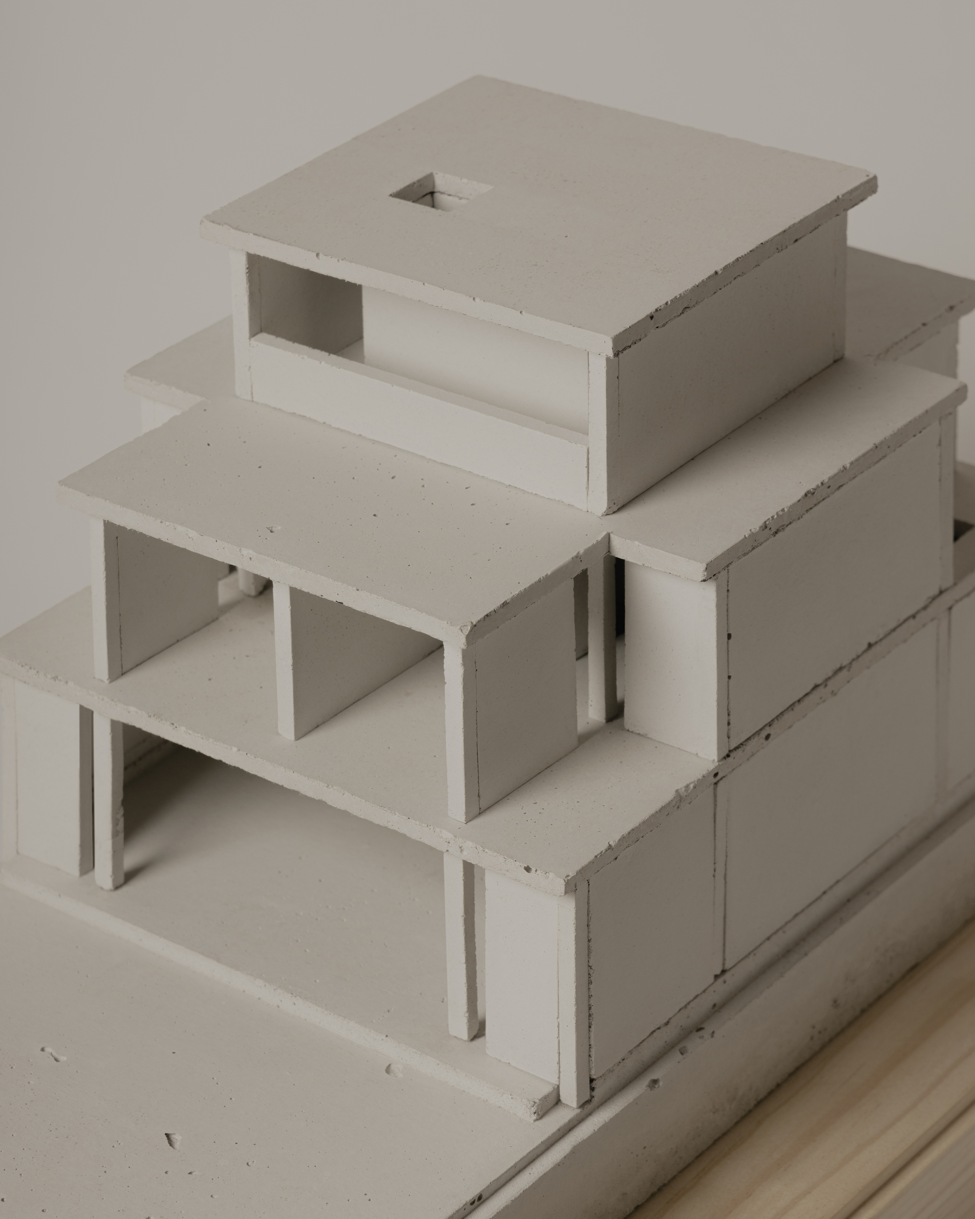 Physical model showing tiered volumes with open terraces and a central skylight on a timber base
